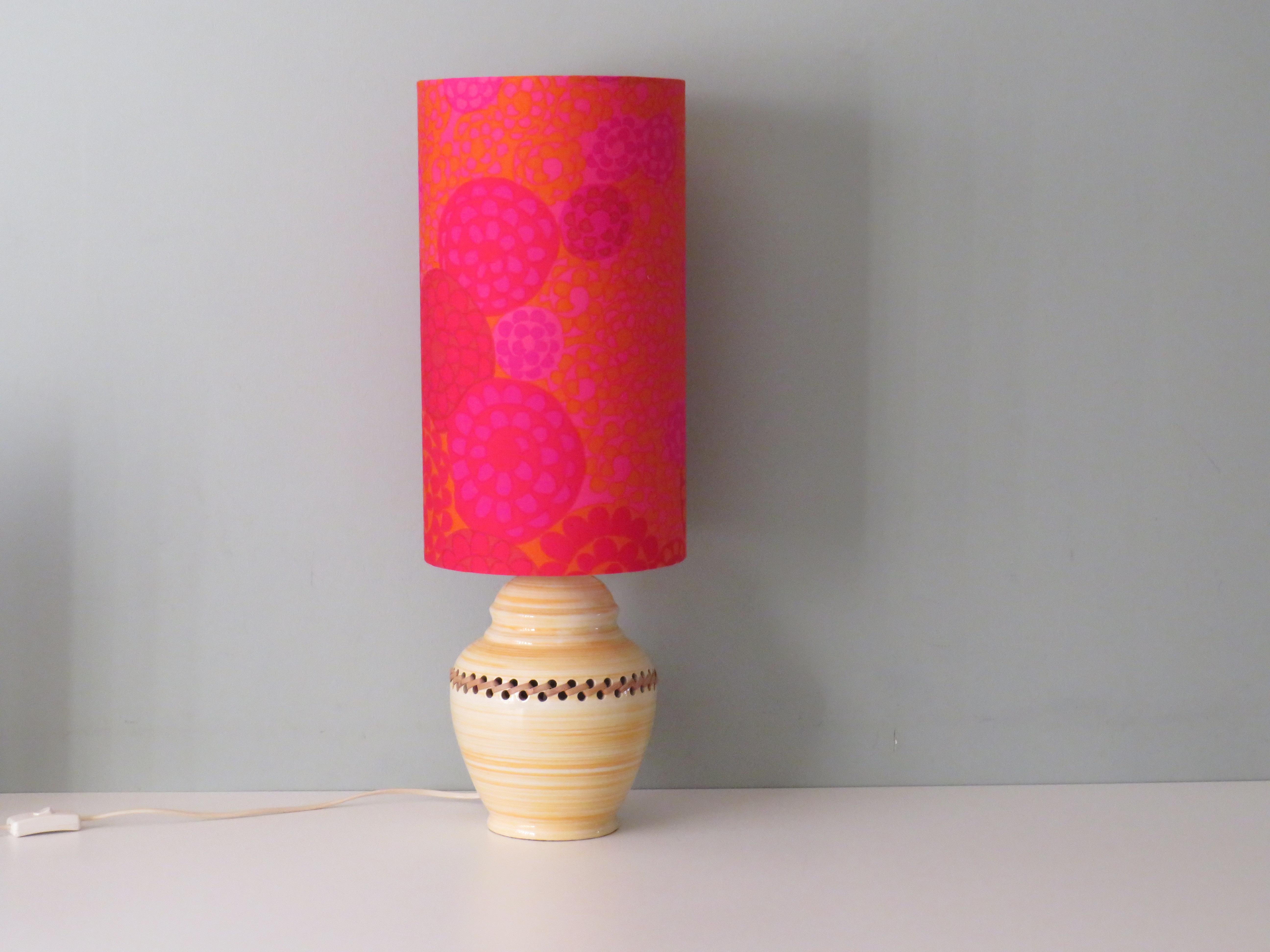 Pied de lampe en céramique émaillée à motif de rayures blanches et jaunes, finition en rotin.
L'abat-jour est fabriqué sur mesure à partir d'un tissu en coton vintage avec un motif floral stylisé dans des tons de jaune, orange, rose et