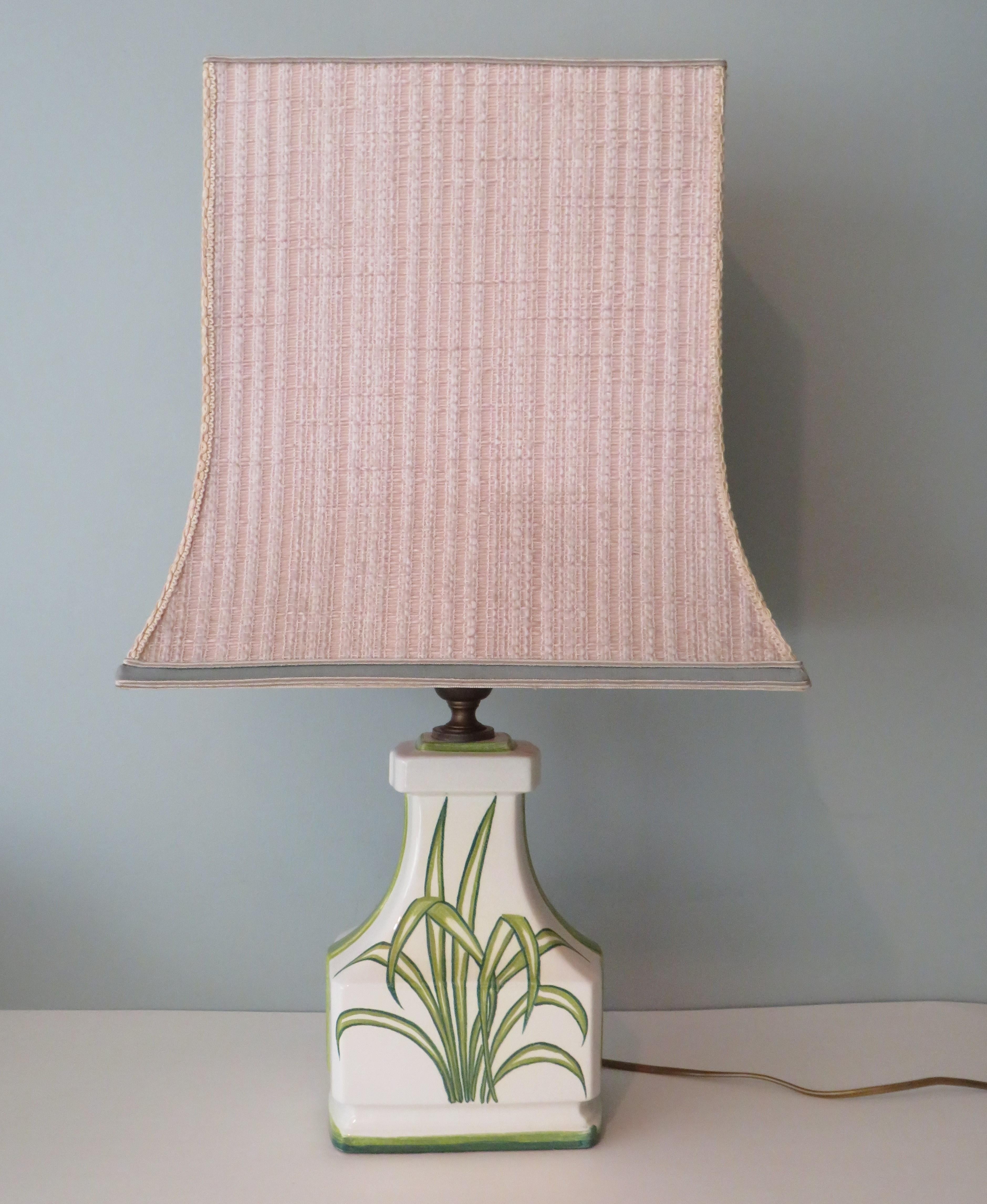 Large white ceramic table lamp with a palm leaf motif in different shades of green.
The lamp has a brass armature and a pagoda shaped lamp shade. The shade is made of ecru woven fabric and trimmed with velvet.
The cord, the on and off button and