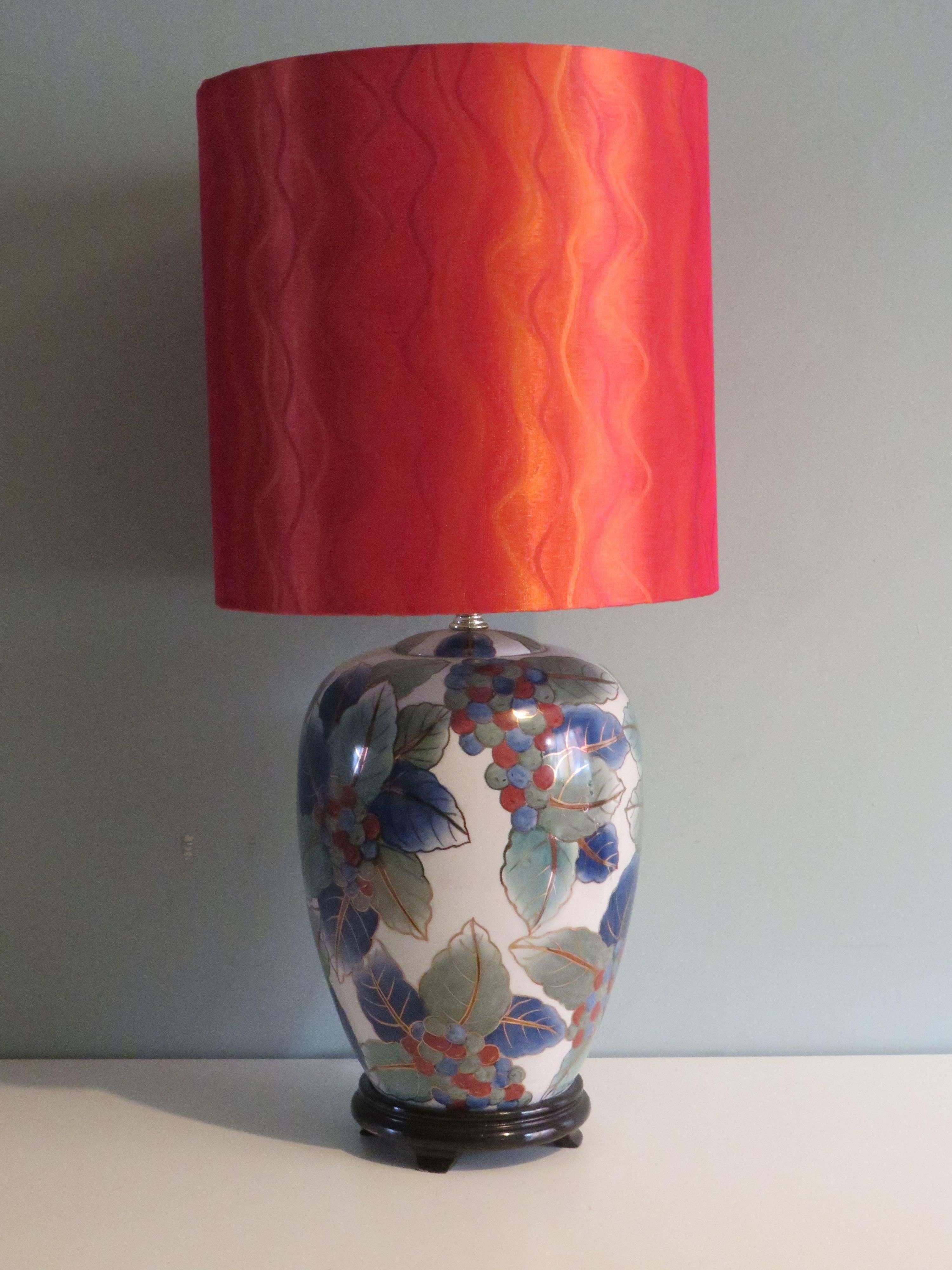This beautiful table lamp features a leaf and berry motif in blue, green and orange-brown tones finished with a gold rim on a white background. The lamp base is mounted on a black wooden base.
The vintage lamp base is equipped with a new,