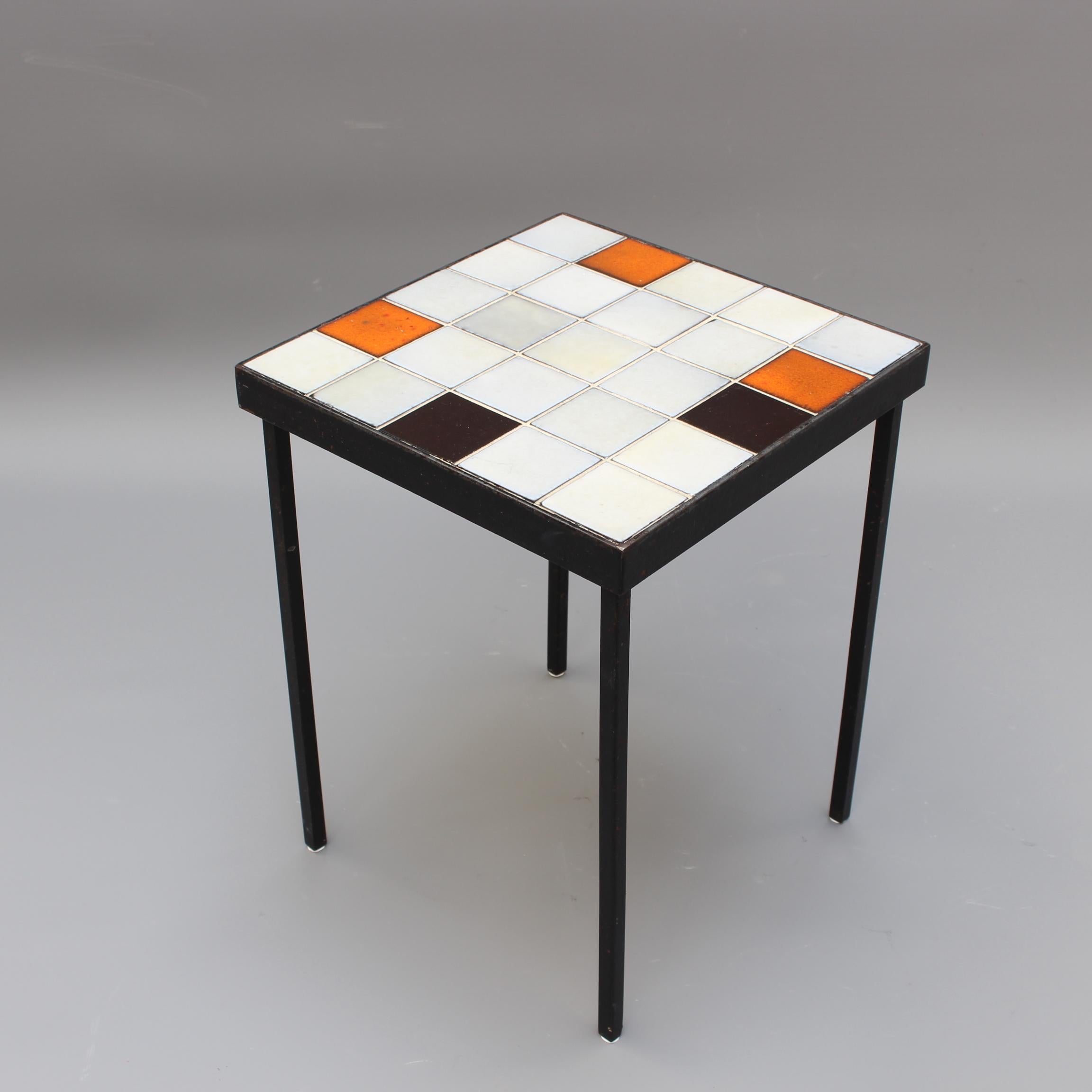 Small side table perfectly simple and simply perfect by Mado Jolain (circa 1950s). Ceramic tiles sit upon a frame and black metal legs in elegant symmetry. The tiles are an eclectic mix of off-whites, black and orange. The end result is a harmonious