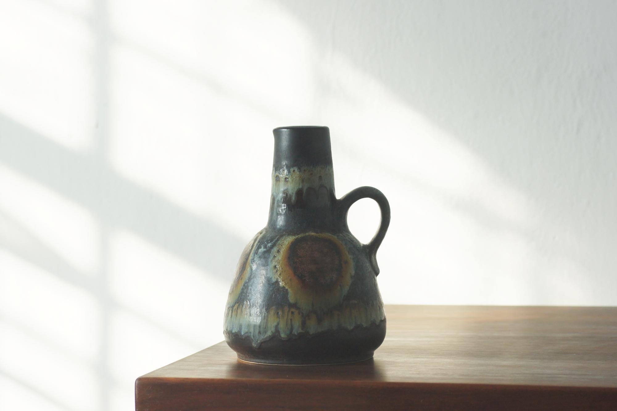  A rare collector's vase from the legendary German manufacturer Dümler & Breiden, model number 1054/22, presents a combination of raw form and expressive glaze characteristic of the mid-century modern era.

The vessel is made of dark, heavy ceramic