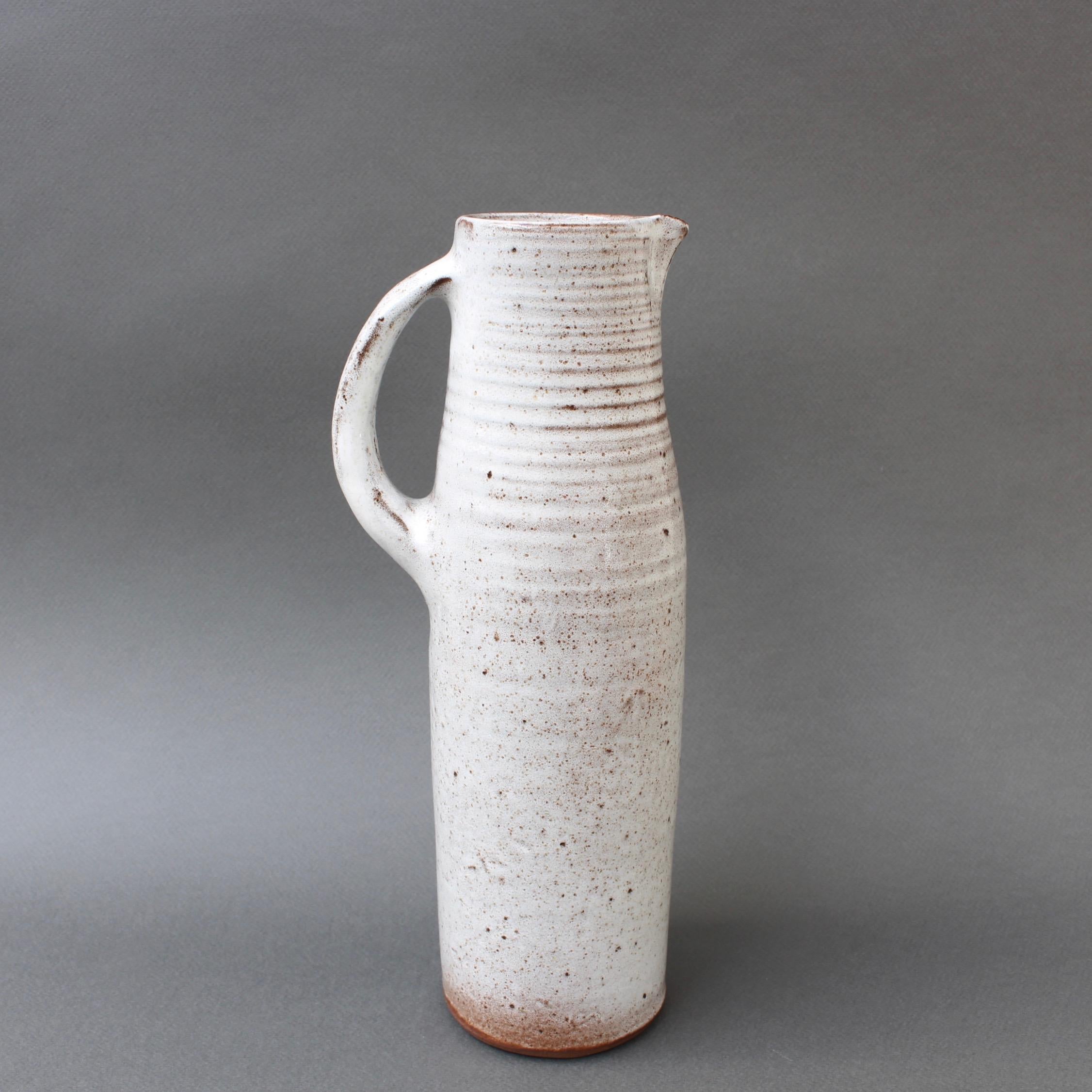 Midcentury French ceramic vase / jug by Jeanne & Norbert Pierlot (circa 1960s). With an off-white base and sandstone accents, this elongated and elegant vase with handle and spout is a delight. The glazed parts that are predominantly white are