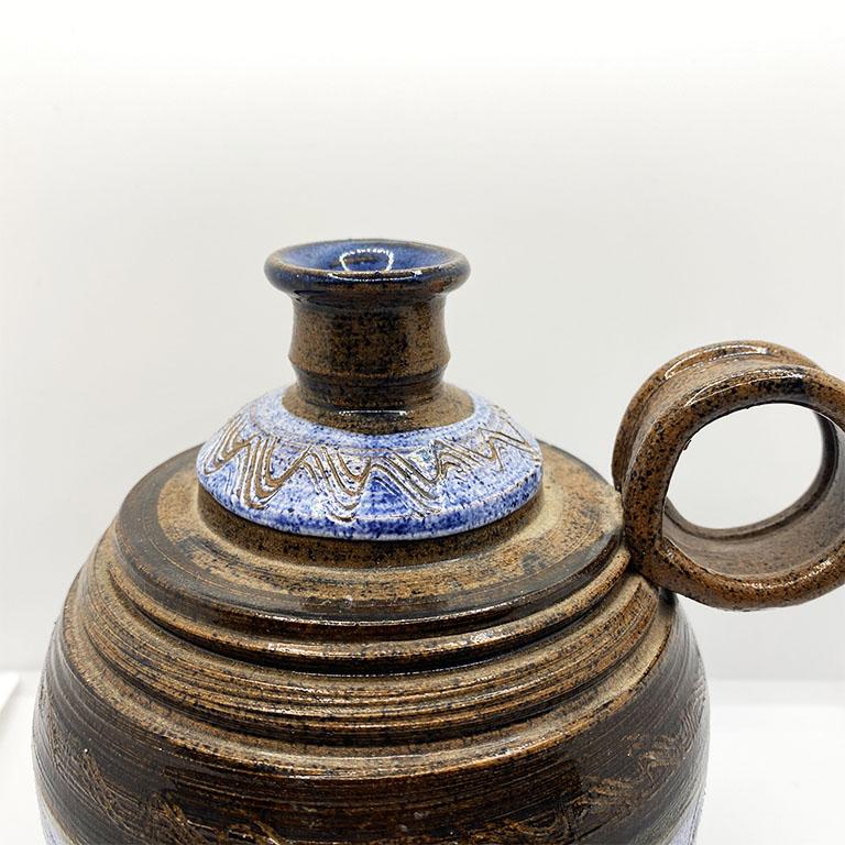 A unique ceramic jug or vase with a handle. This piece is created from ceramic and circular in form. The body is decorated in a textured blue and brown design. The neck is narrow, and glazed on the inside making it perfect for use as a vase or