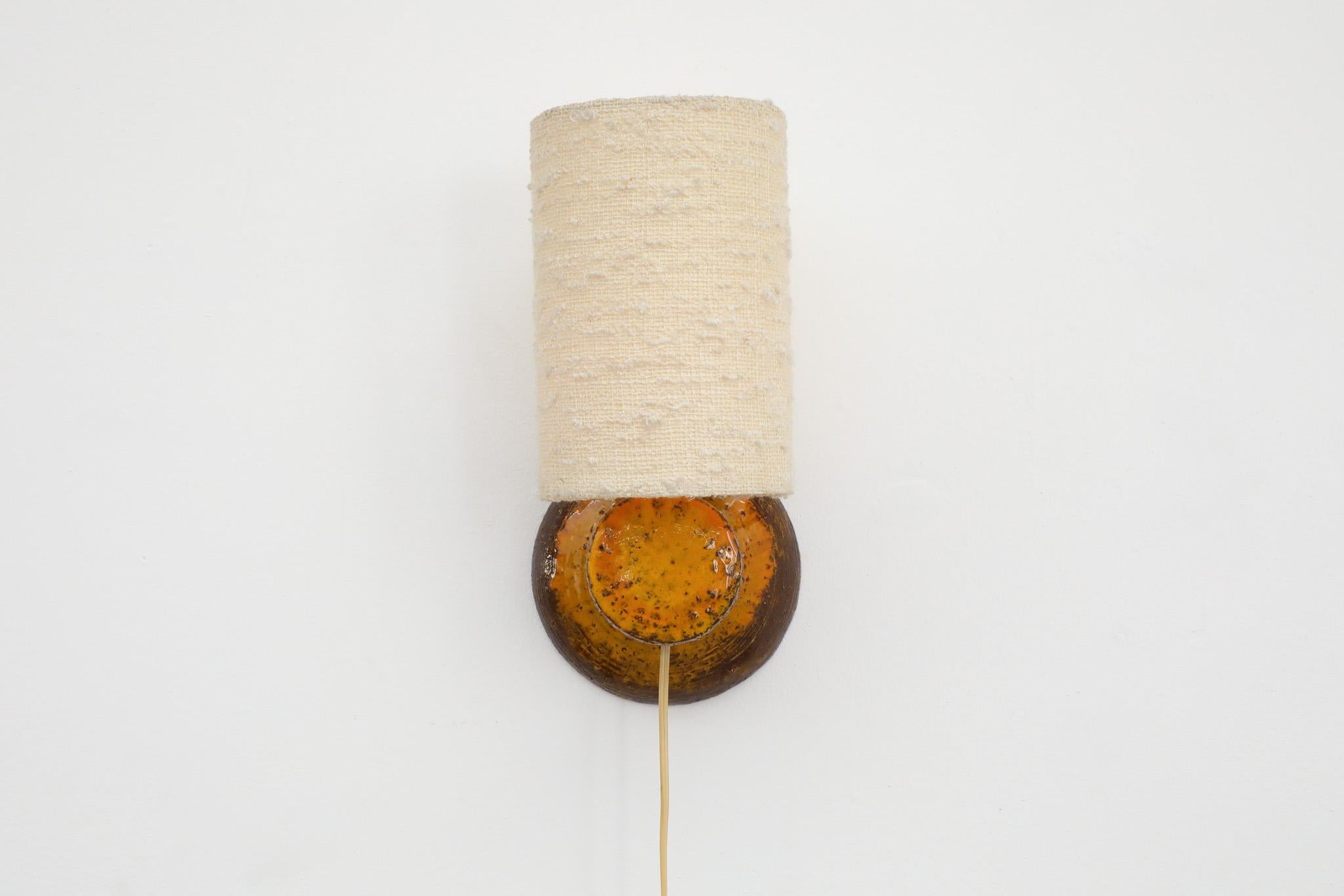 Mid-Century, ochre and brown glazed, 1970s ceramic wall sconce complete with small linen drum shade. In original condition with some visible wear consistent with its age and use. Single E26/27 bulb.