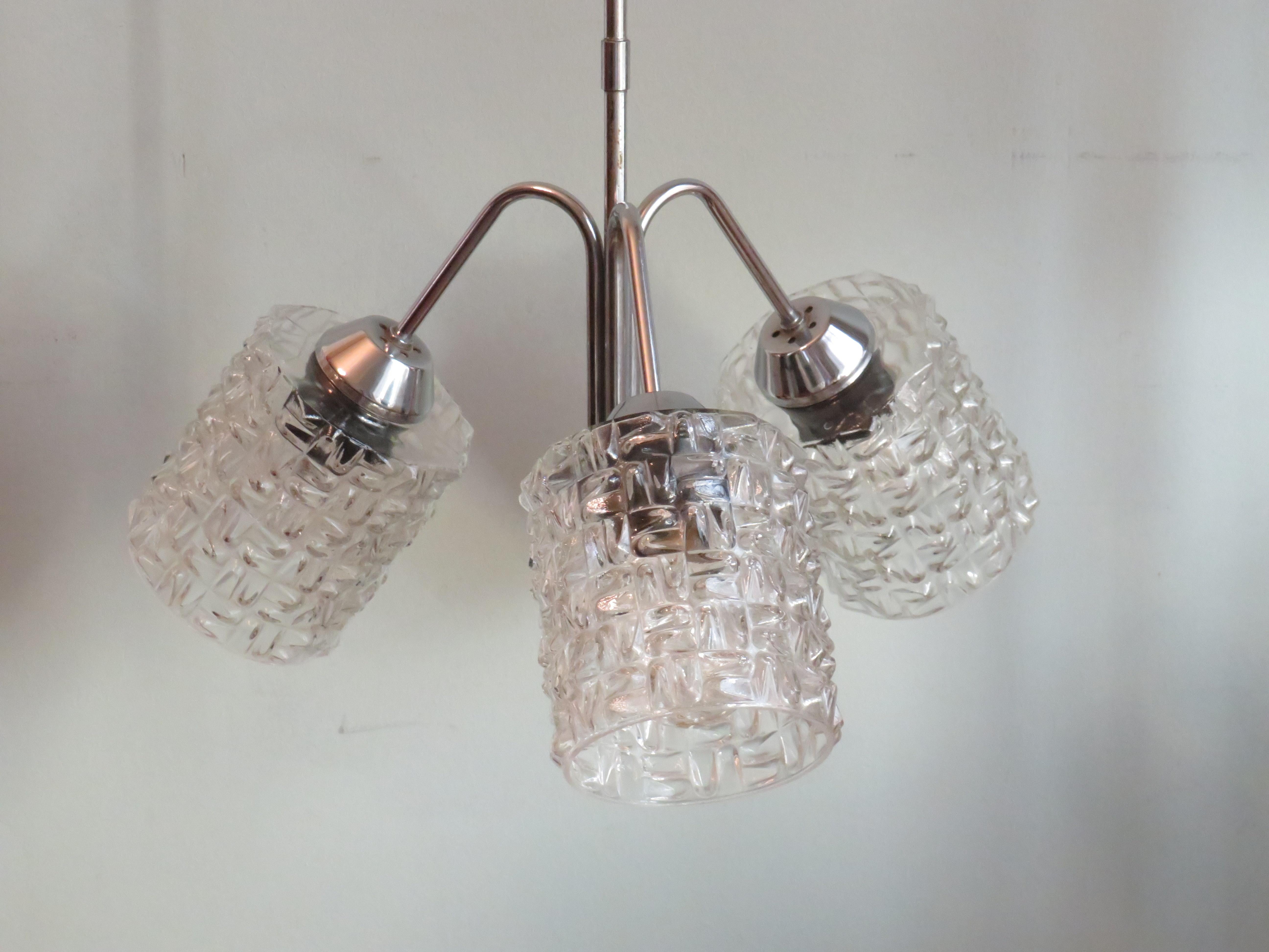 Lampadario a 3 bracci con struttura in metallo cromato e calici in vetro con un bellissimo motivo grafico.
3 prese E27. Il lampadario è dotato di una calotta cromata e di un sistema di sospensione.
L'altezza del lampadario è di 90 cm. La larghezza