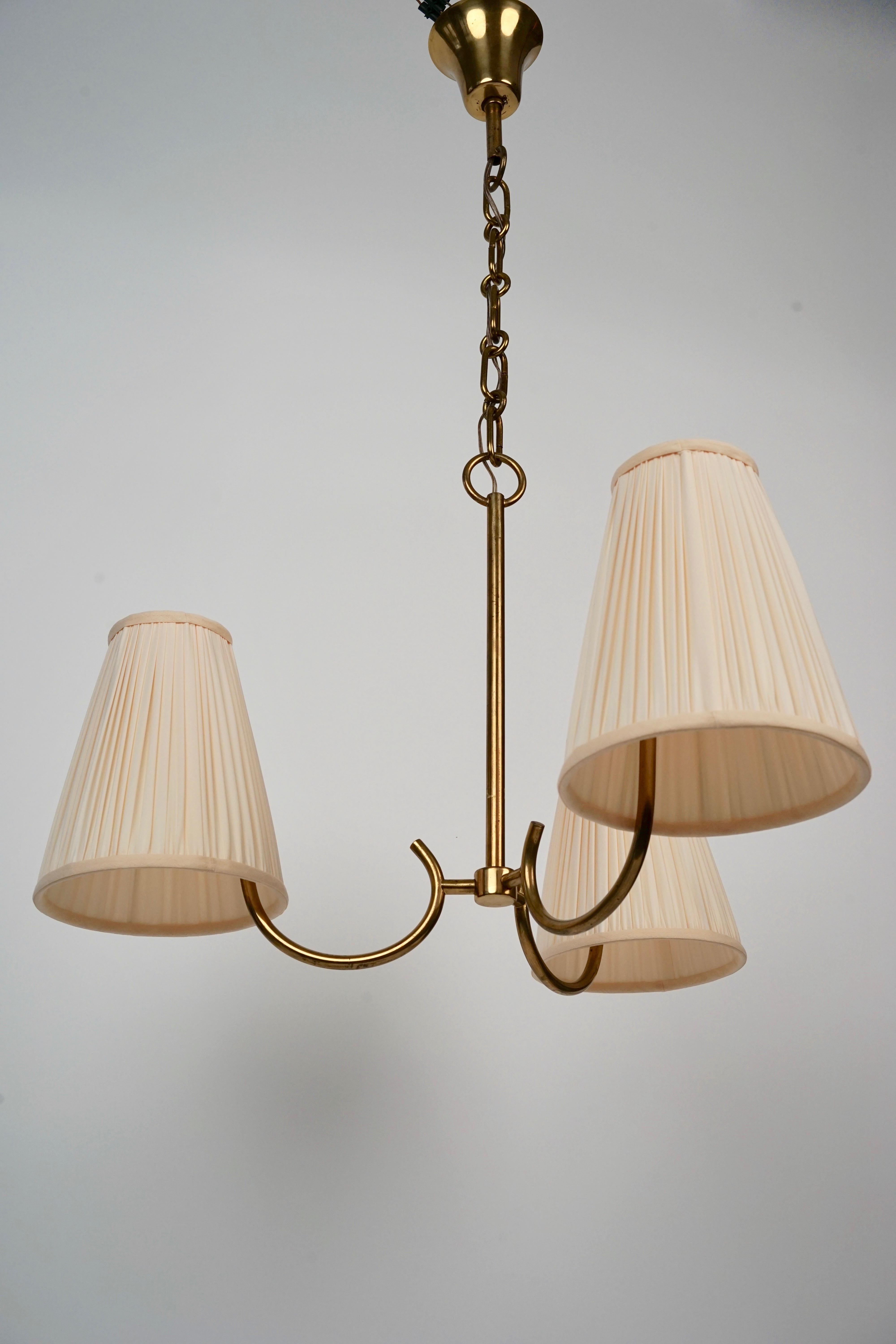 Three arm brass chandelier made in Austria from the firm Rupert Nikoll, in a decorative style from the 1950's. The three arms are decorated with new cream coloured silk shades matching the originals.