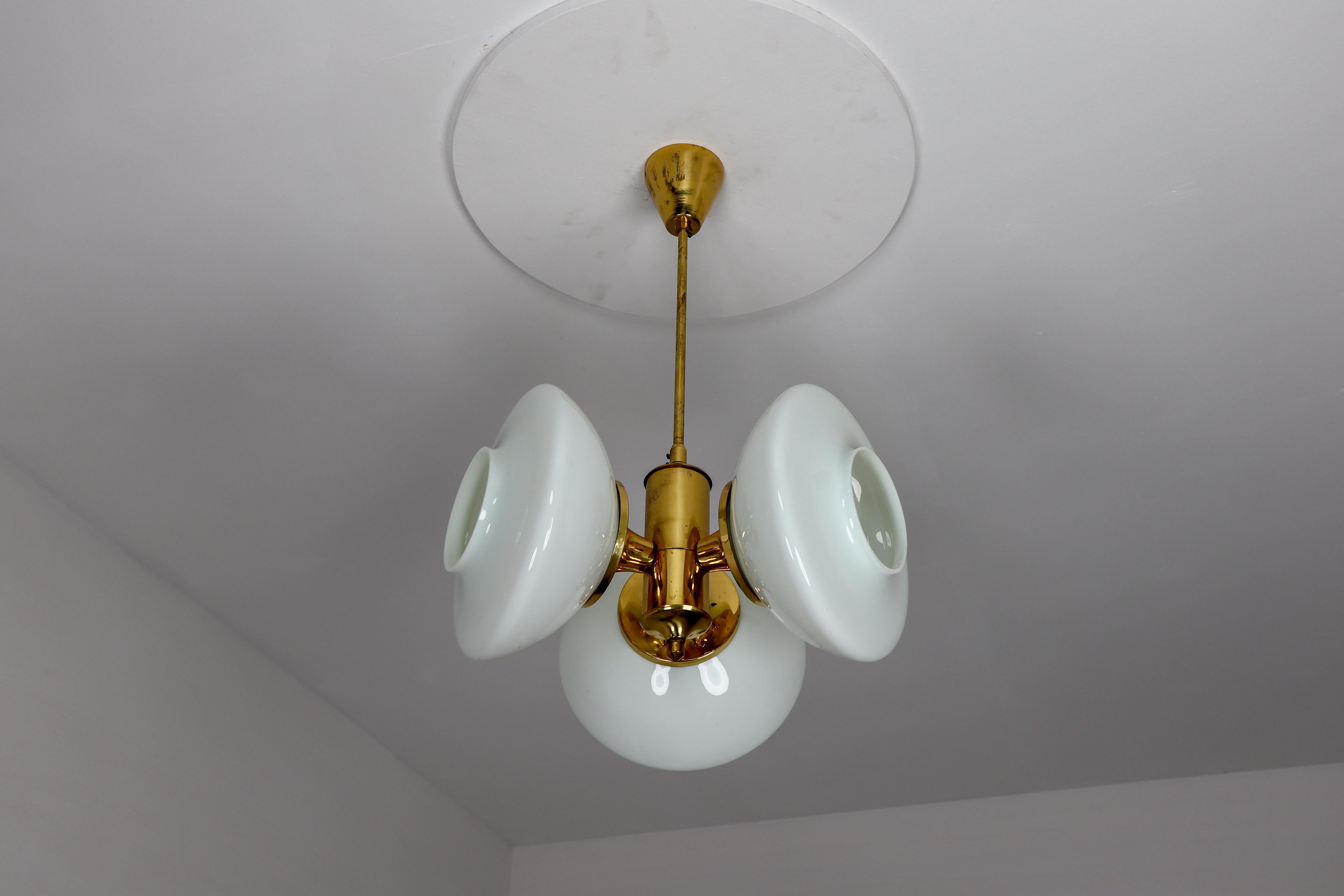 Midcentury chandelier with brass fixture and opaline glass. This chandelier with brass frame consist of three lights. The diffuse light it spreads is very atmospheric. Completed with the opaline glass and brass details, this chandelier will