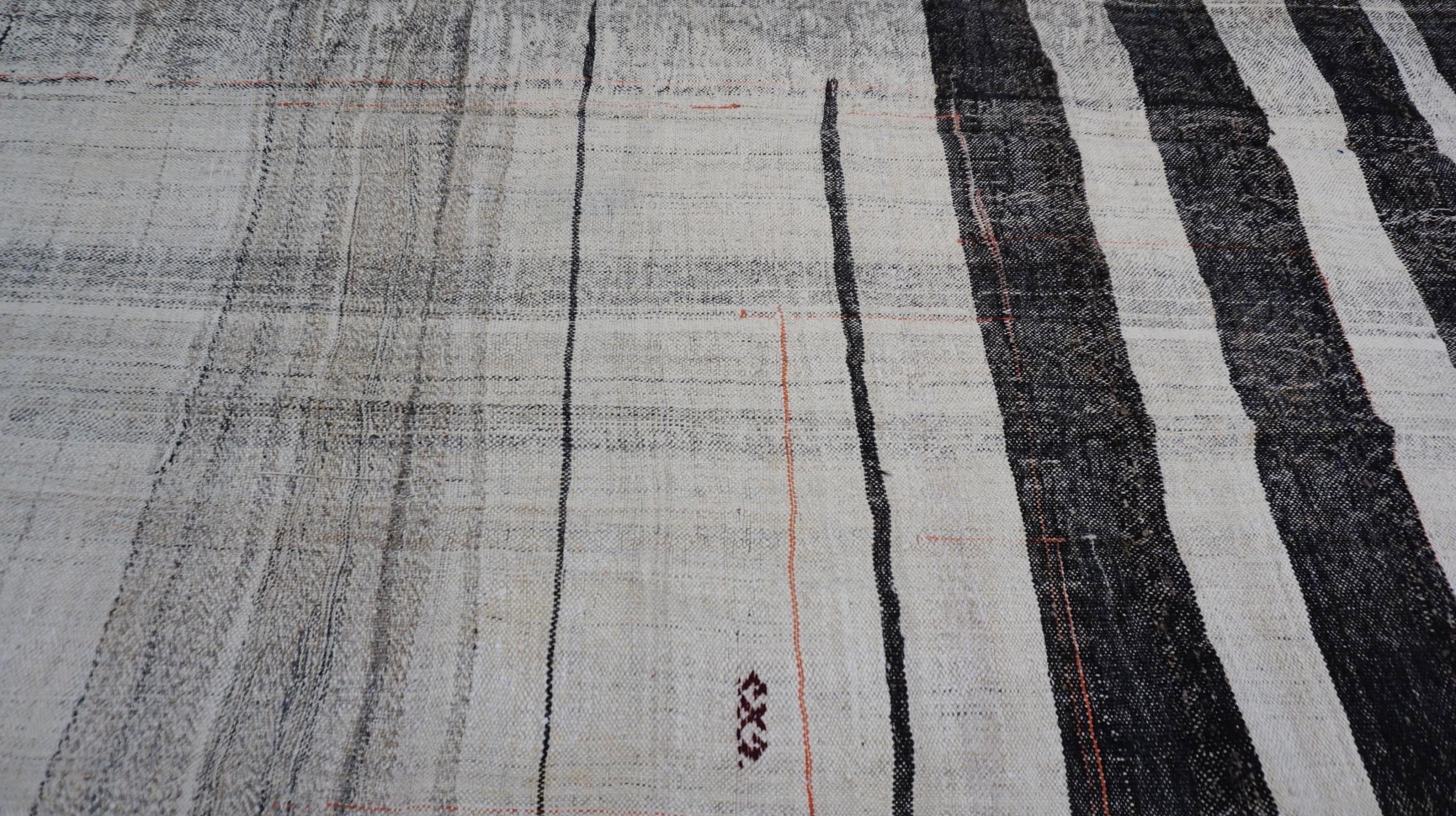 This vintage kilim showcases an abstract interplay of irregular stripes and organic tonal variations in a sophisticated neutral palette. The juxtaposition of horizontal and vertical patterns creates a striking, modern aesthetic, making this piece a