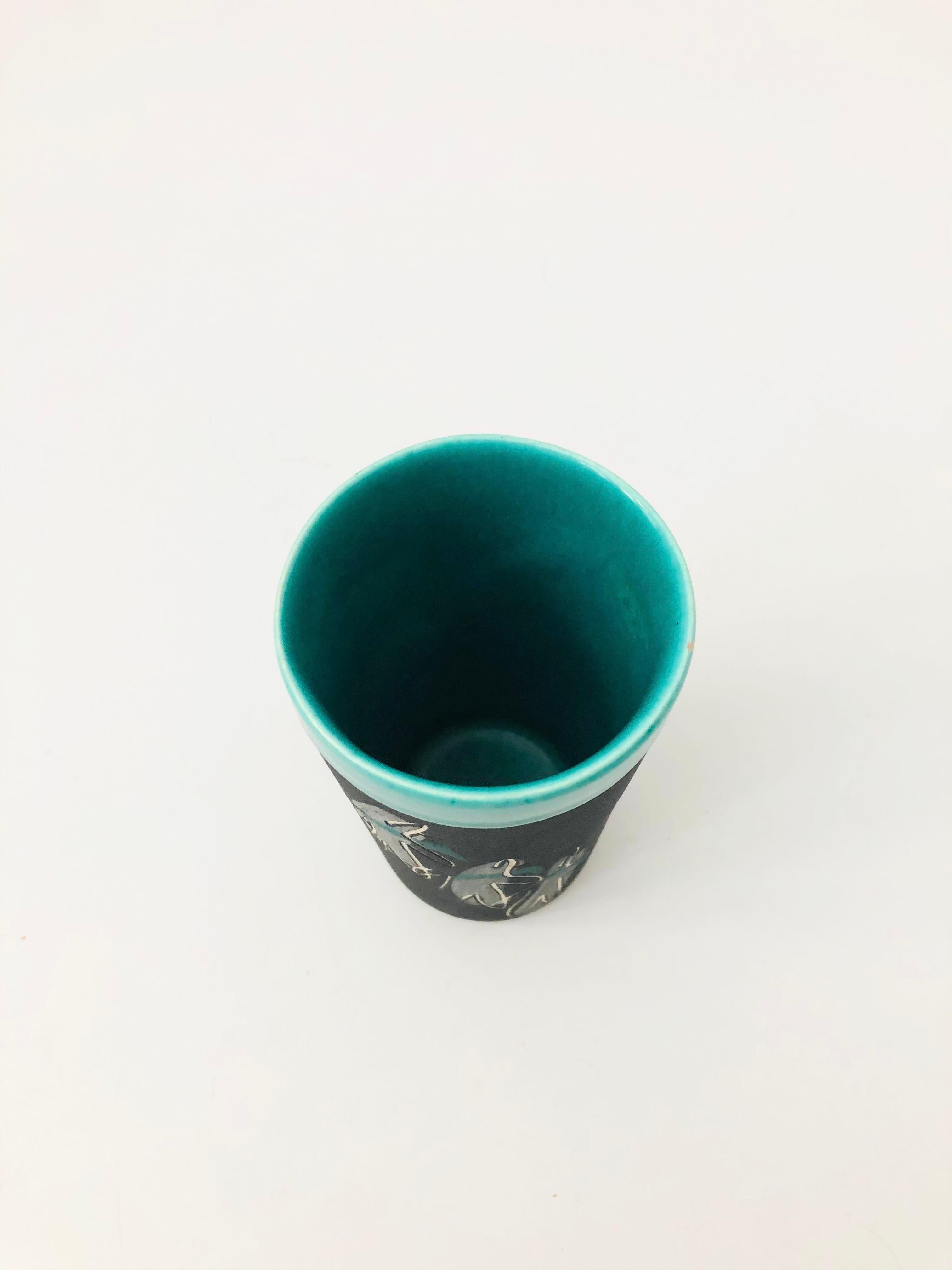A wonderful midcentury studio pottery tumbler from the 1940s-1950s by ceramicists, Charles and Alice Smith of California. Decorated with a series of figures carved into the sides of the mug. Finished in a matte black glaze with a glossy green glaze