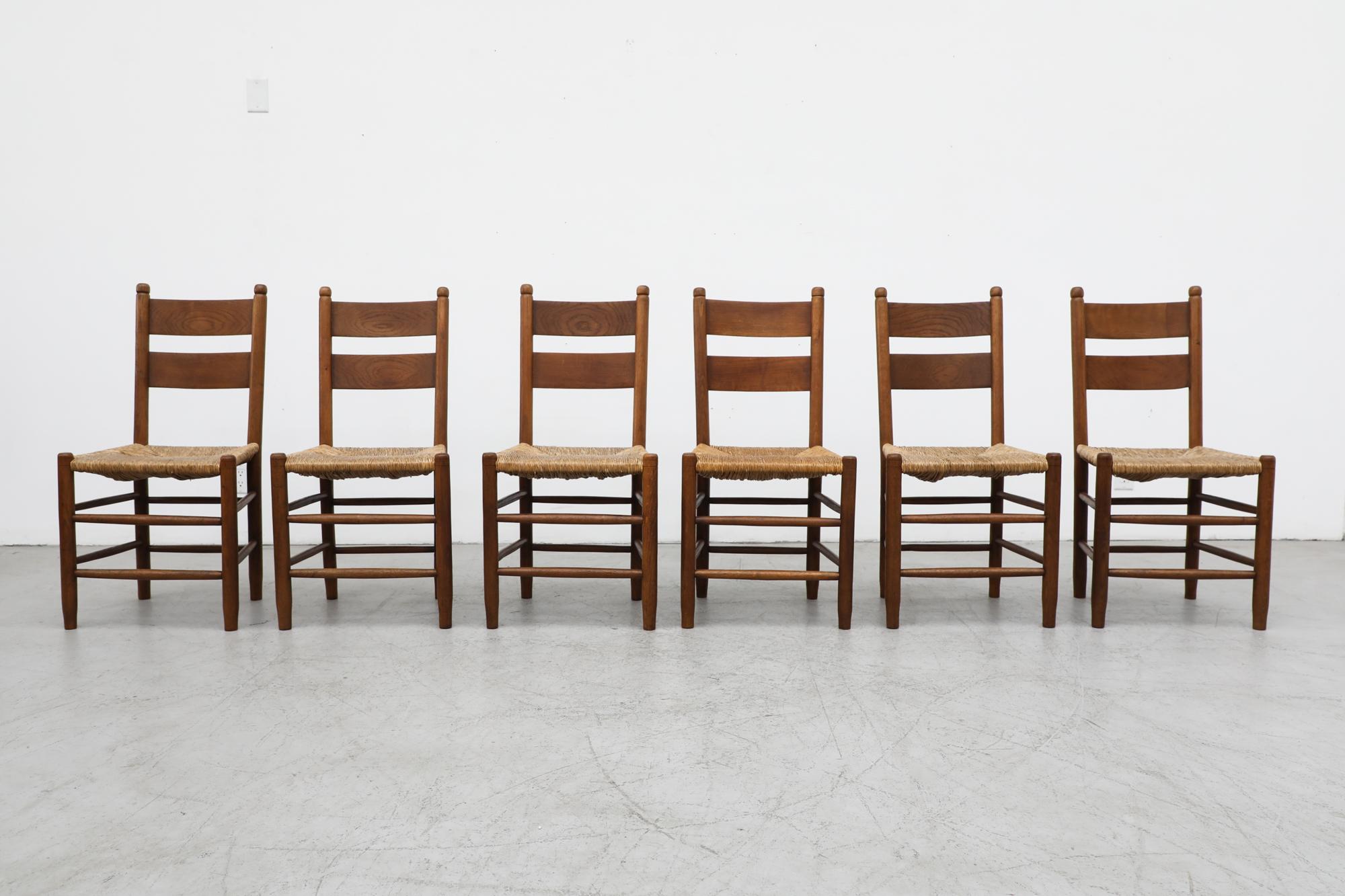 Quaker Style ladder back dining chairs in the style of Charlotte Perriand with dark stained oak frames and rush seats In original condition, with visible patina and heavy wear, including some breakage and loss to rush seats. Wear is consistent with