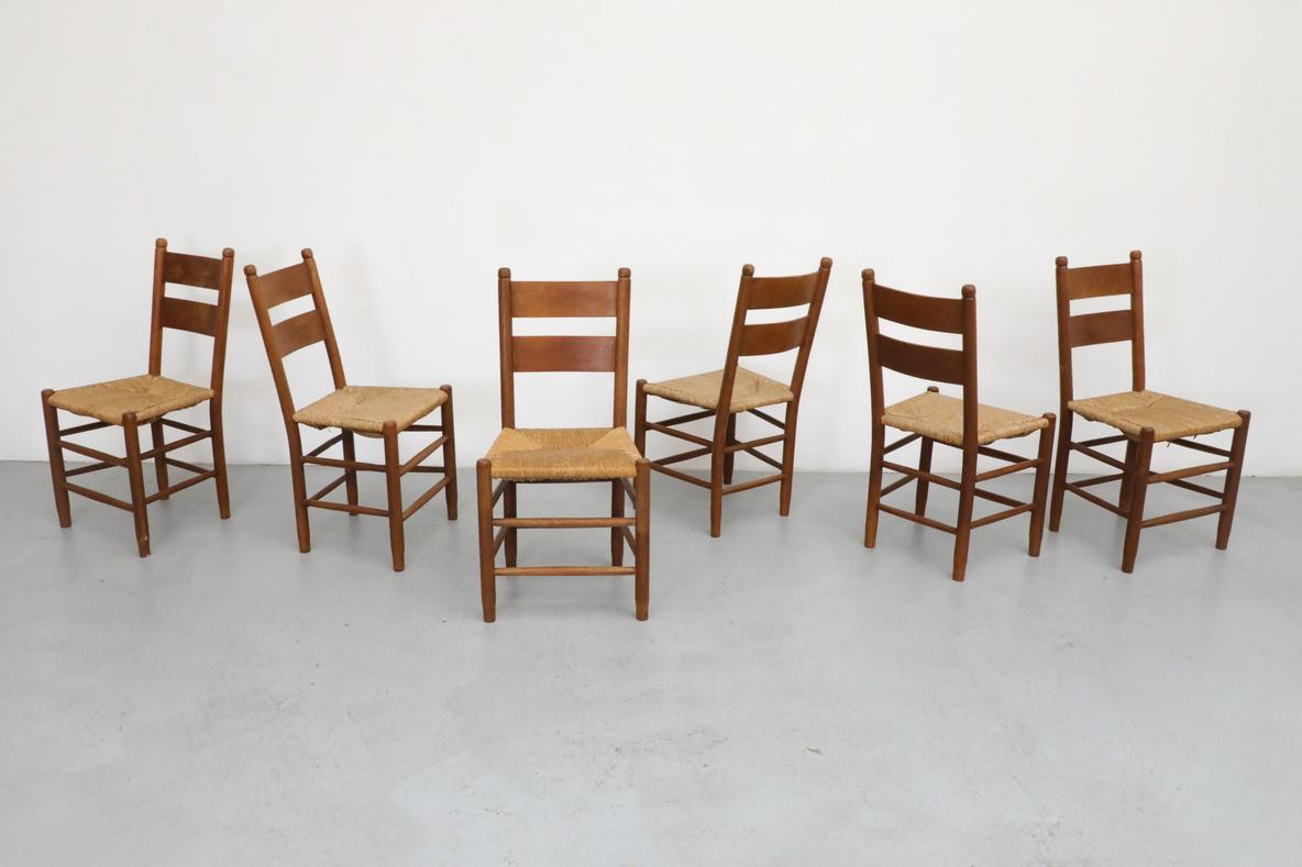 Quaker Style ladder back dining chairs in the style of Charlotte Perriand with lightly refinished dark stained oak frames and rush seats In original condition, with visible patina and heavy wear, including some breakage and loss to rush seats. Wear