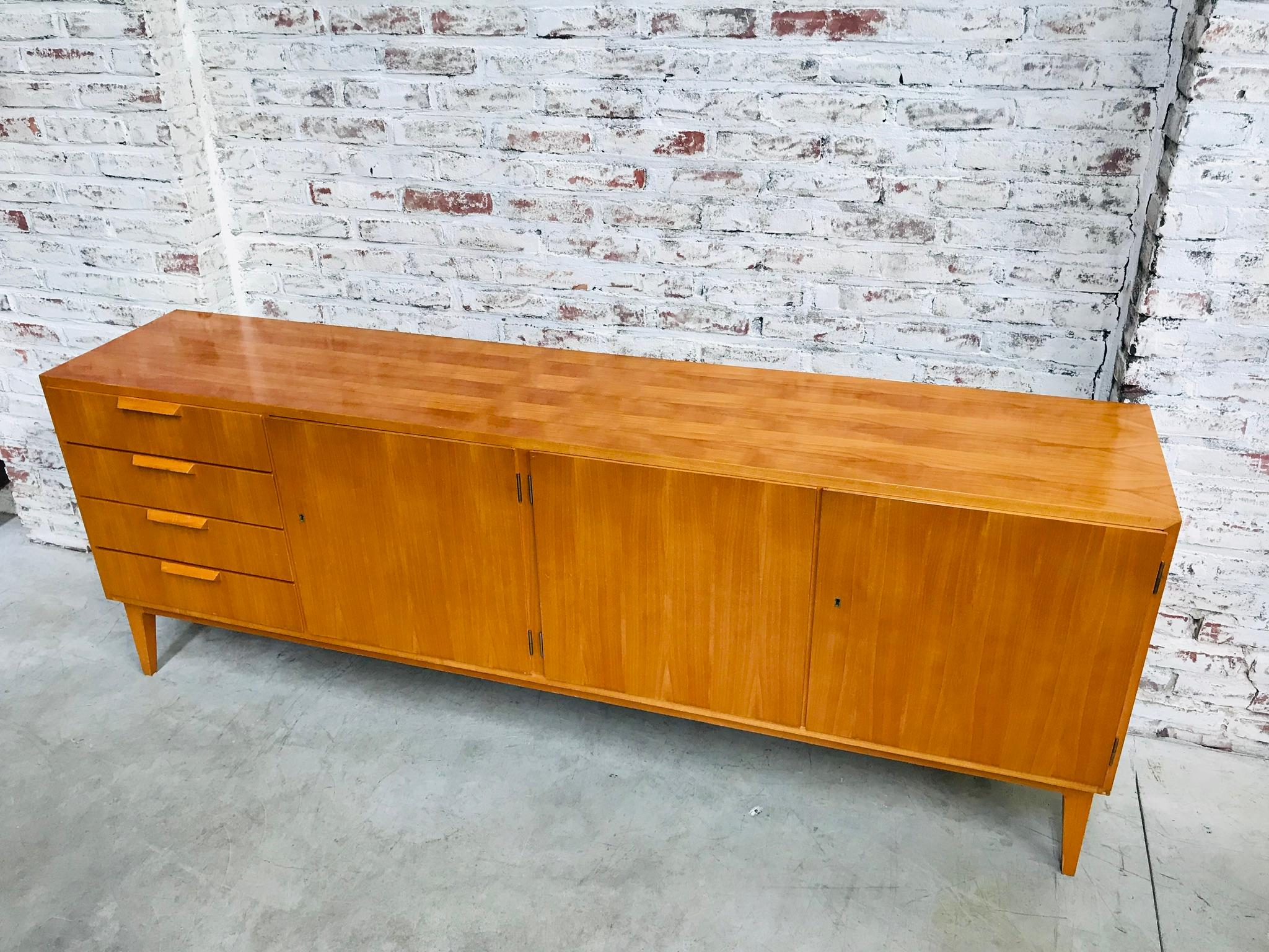 This sideboard was manufactured in West-Germany in the late 1960s. The maker used a special technique in woodwork in order to create a “checkered” surface on the front of the sideboard. If you look on the top and both sides you see the French
