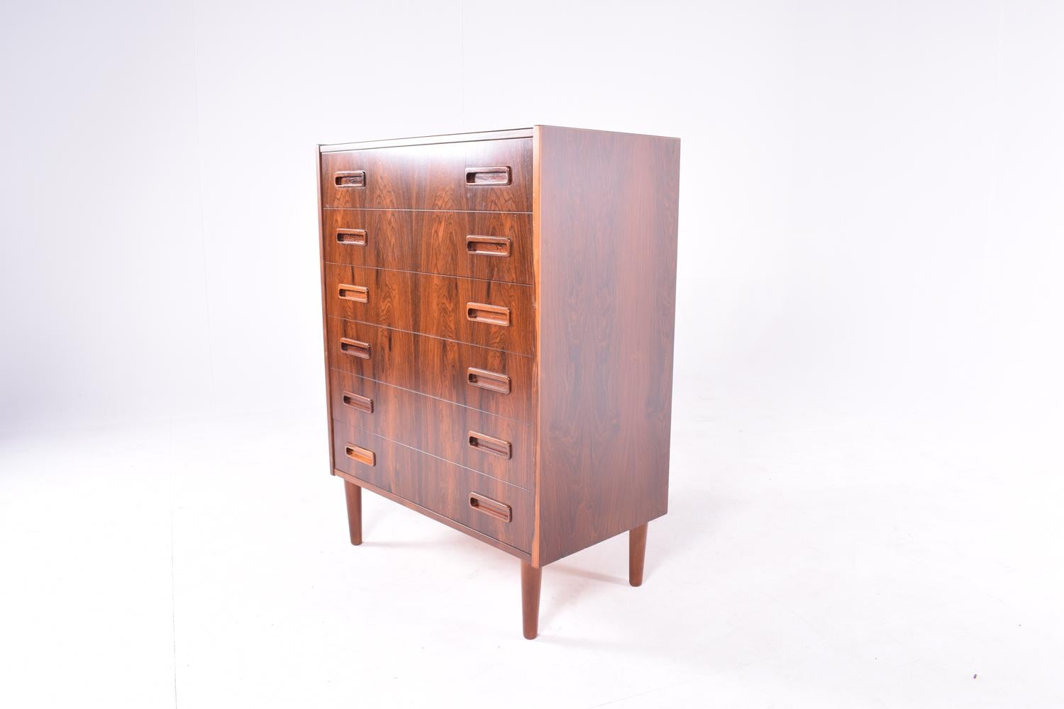 Midcentury rosewood chest of drawers with six front drawers and round tapered legs.
Exceptional veneer and amazing craftsmanship on the handles. A piece of excellence to add to your bedroom decoration.