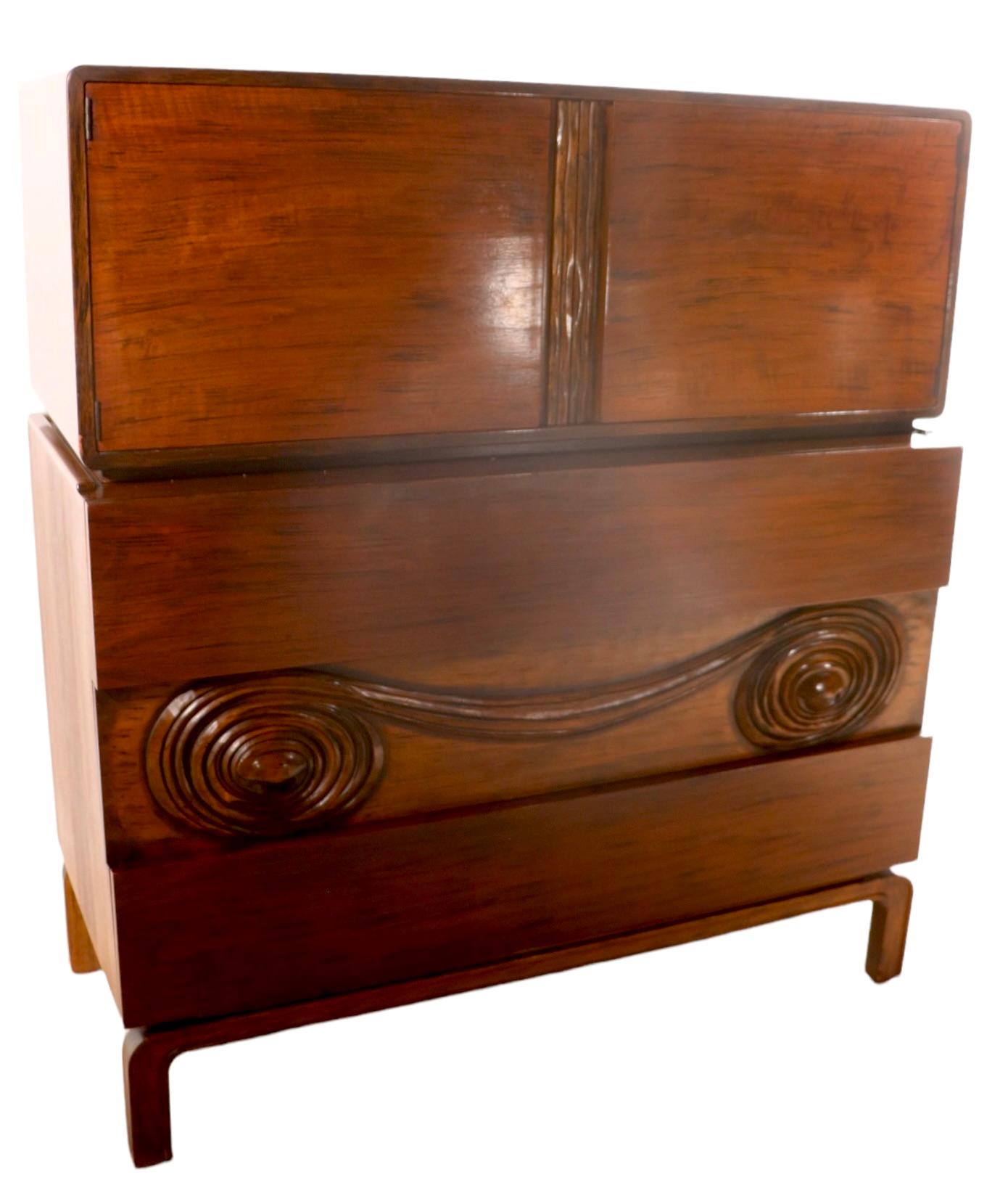 Very unusual and rare two part chest on chest, made in Sweden, c 1950’s, designed by Edmond Spence. Executed in exotic Macassar veneer, with dramatic carved front panel.
         