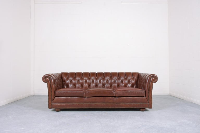 An extraordinary vintage mid-century chesterfield sofa is crafted out of wood and leather combination in great condition and completely restored by our professional craftsmen team. This sofa features the original leather upholstery newly dyed in