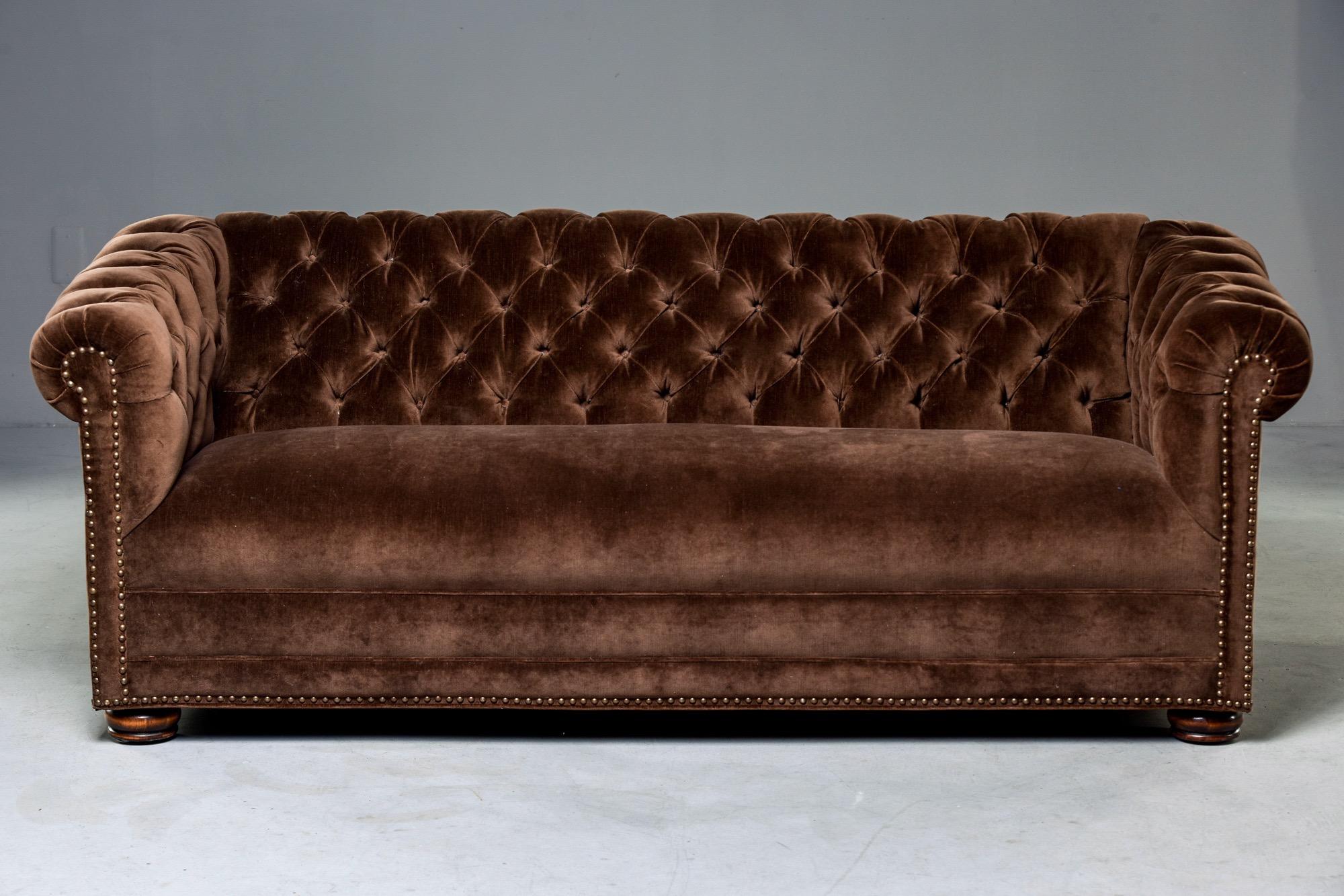 Classic Chesterfield sofa features tufted seat back and rolled arms, bun feet and dark brass nailhead trim, circa 1970s. Newly upholstered in chocolate brown velvet. Unknown maker. Sofa is high quality with solid construction and smaller, versatile