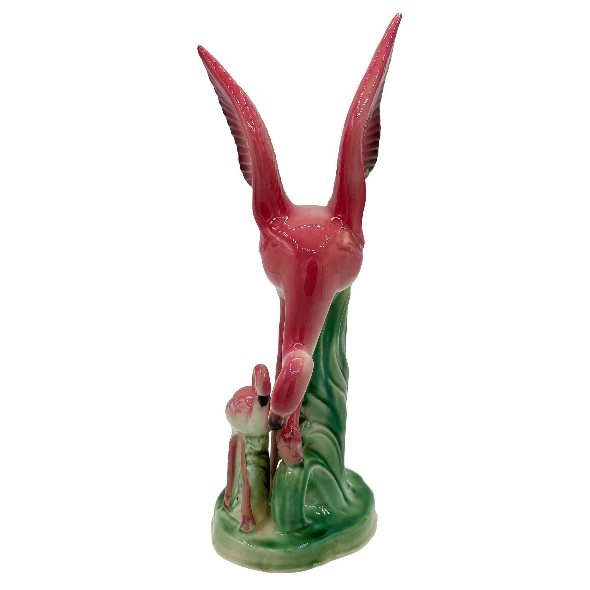 Mid-century pink and green ceramic Mother and child tabletop pottery statue by Leftons. The statue features a beautifully detailed pink mother and daughter flamingo resting on a grassy field. It comes in a gloss finish that highlights the rich