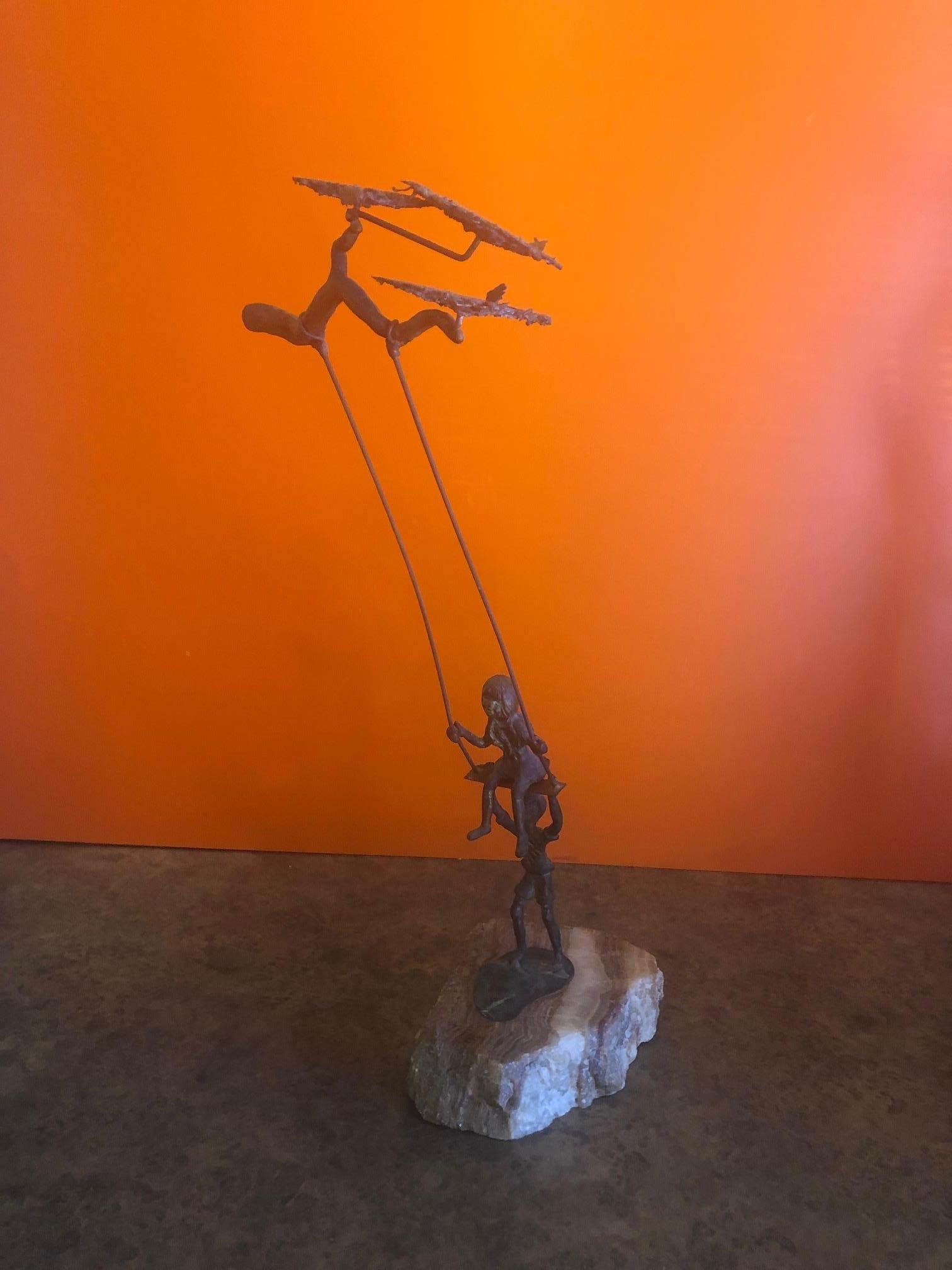 Beautiful patinated bronze sculpture of a young boy pushing a young girl on a tree swing by Bijian. The sculpture sits on a raw piece of quartz stone that is signed. Fun and hard to find piece.