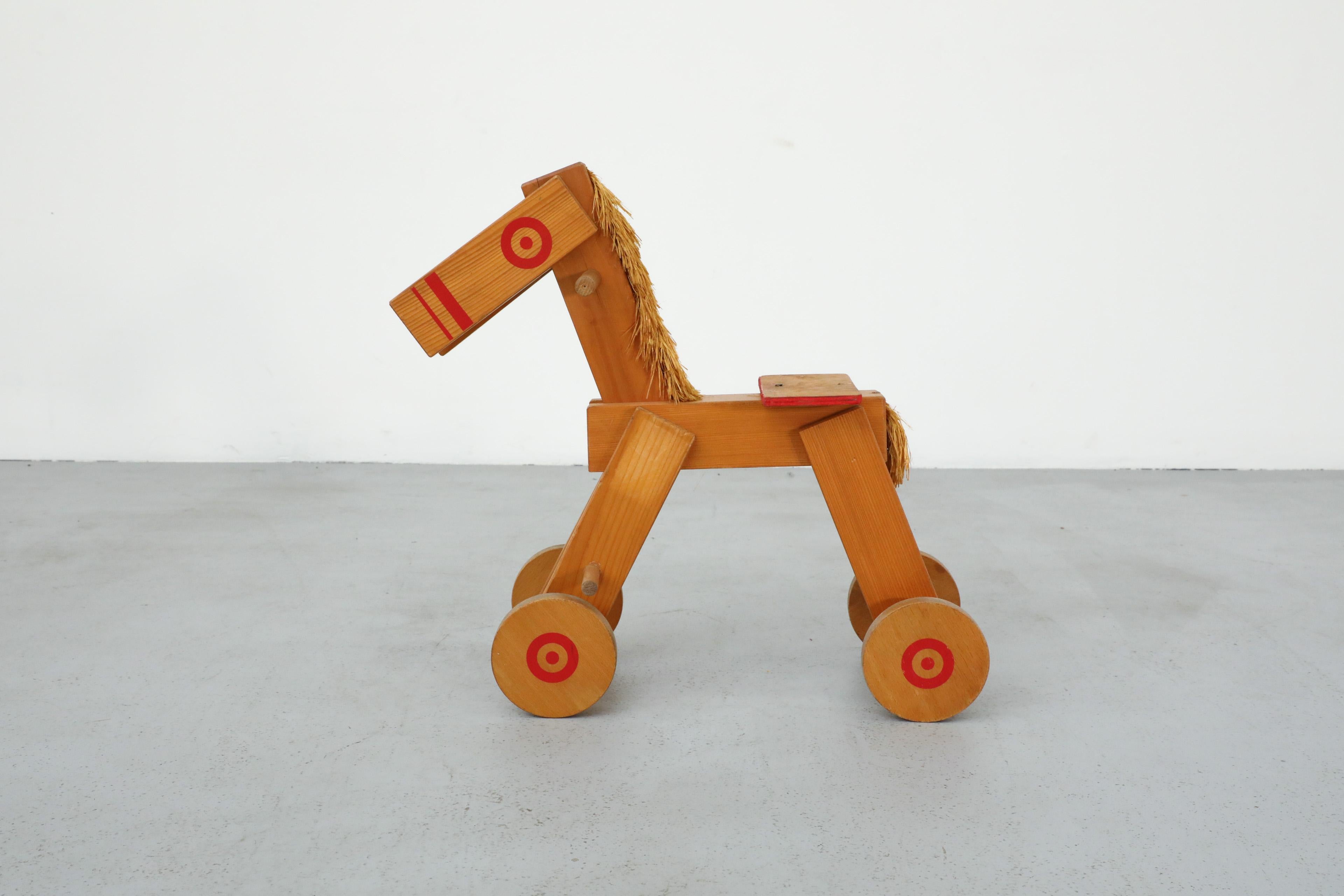 Mid-Century children's wooden pony with wheels, red painted details, handles and straw mane and tail. Perfect for a children's room or nursery. In original condition with visible wear consistent with its age and use.
