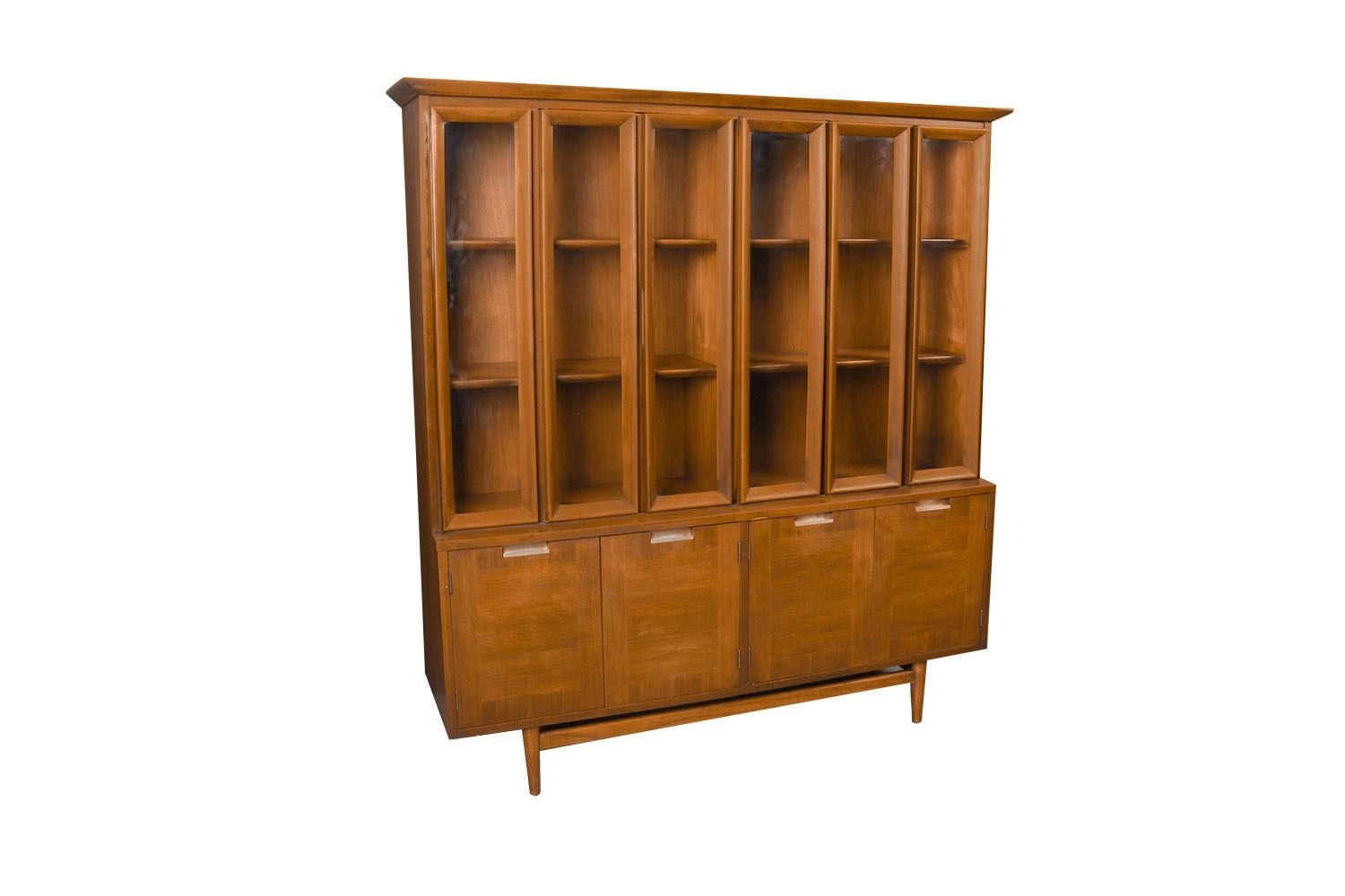 Beautiful, rare, retro Mid-Century Modern detailed proportioned walnut American of Martinsville China cabinet hutch in great original condition. The hutch is one solid-piece, featuring two pairs of stunning bifold glass cabinet paned doors, accented