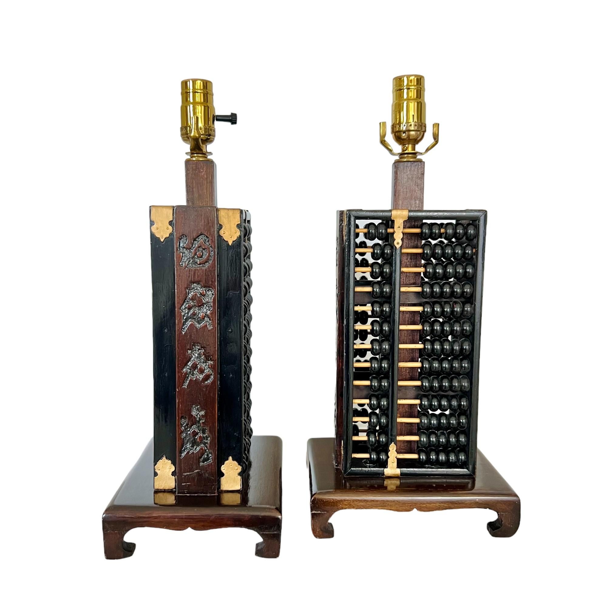 Pareja vintage de lámparas de mesa con ábaco de estilo chinoiserie, hacia 1965. Cuerpo de suanpan de madera lacada y ebonizada por las dos caras, con paneles laterales tallados con caracteres chinos y detalles de metal dorado. 

Ambas están en buen