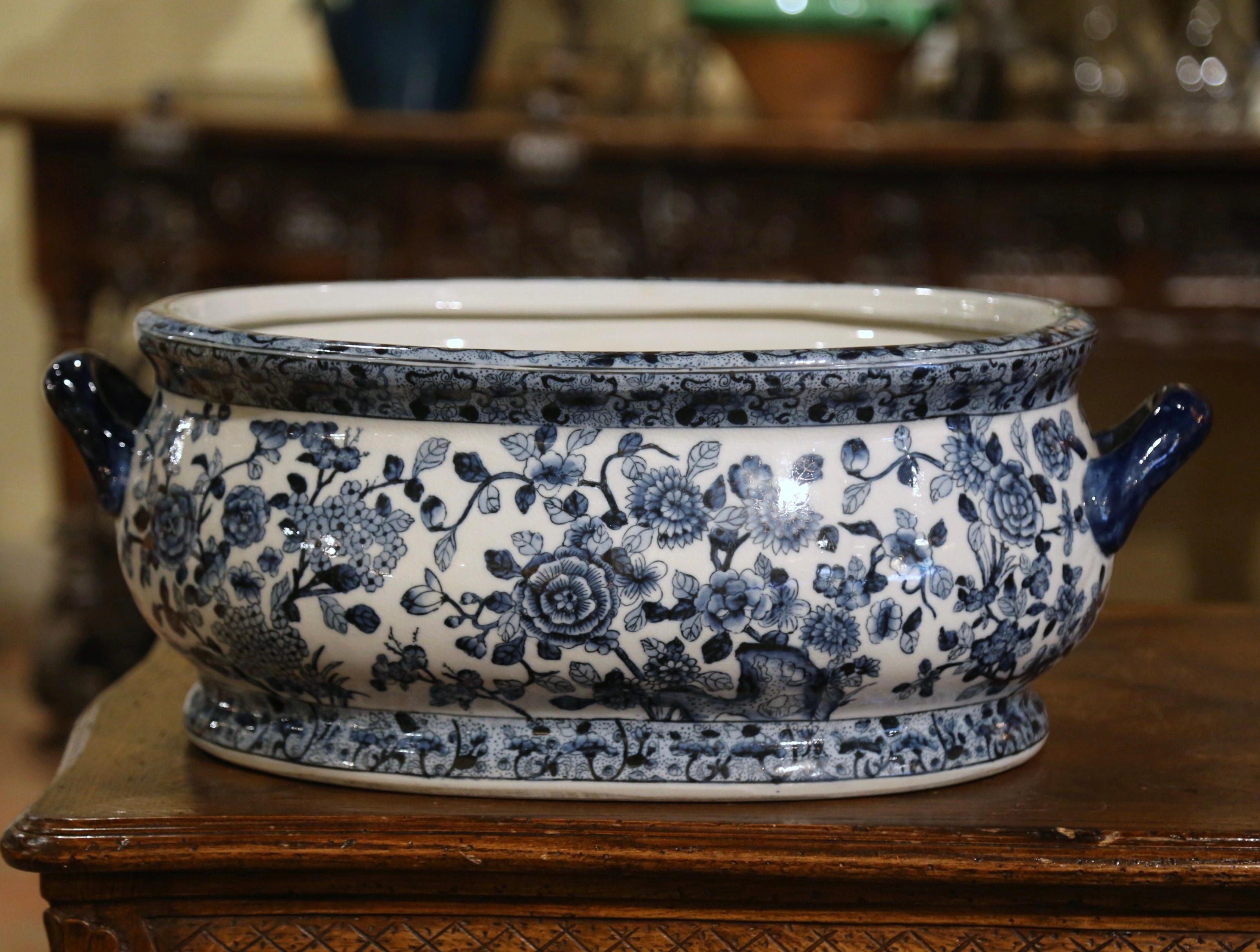 Crafted in China circa 1960 and oval in shape with bombe sides, the vintage porcelain basin is dressed with two side handles; it is decorated with hand painted floral motifs around the perimeter of the pot, the inside features painted fish and
