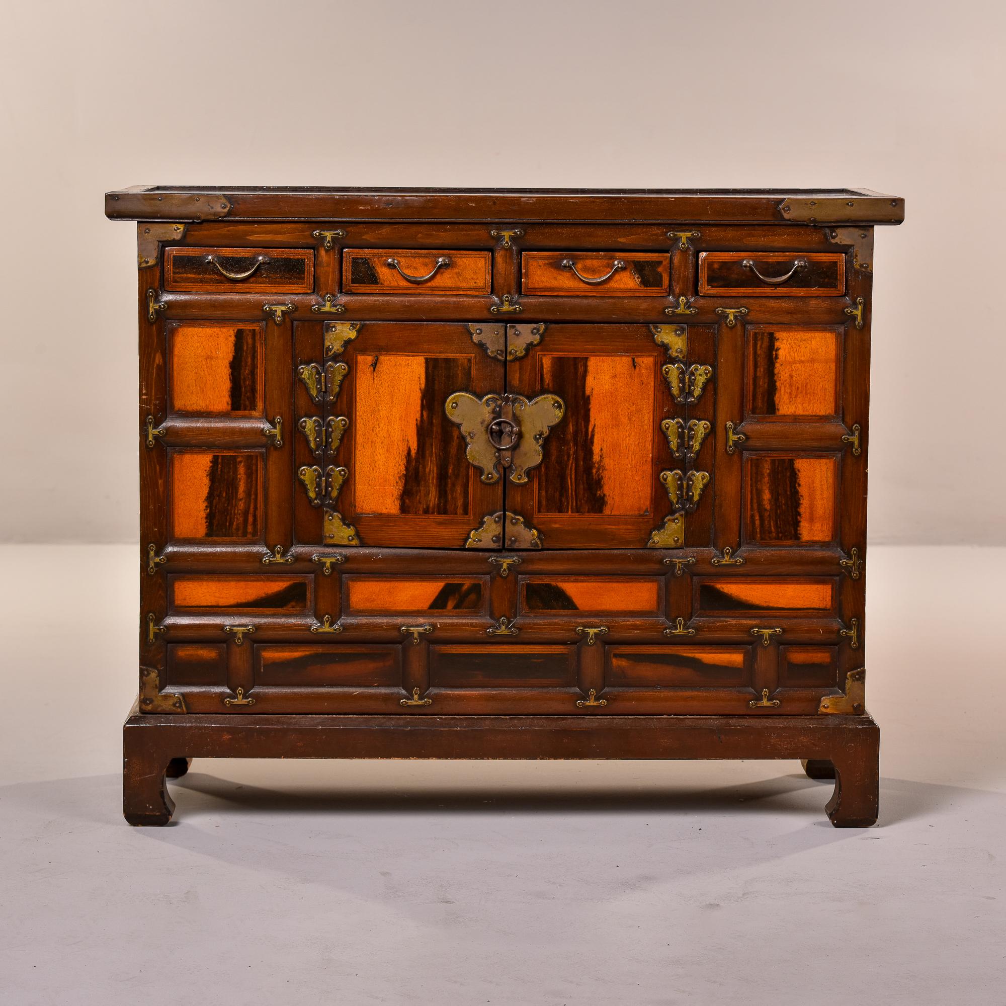 This circa 1950s small Chinese cabinet has four small drawers at the top, chow style feet and an open storage compartment with two hinged drawers. Adorned with decorative brass hardware including butterfly-shaped mounts on the front and wood stained