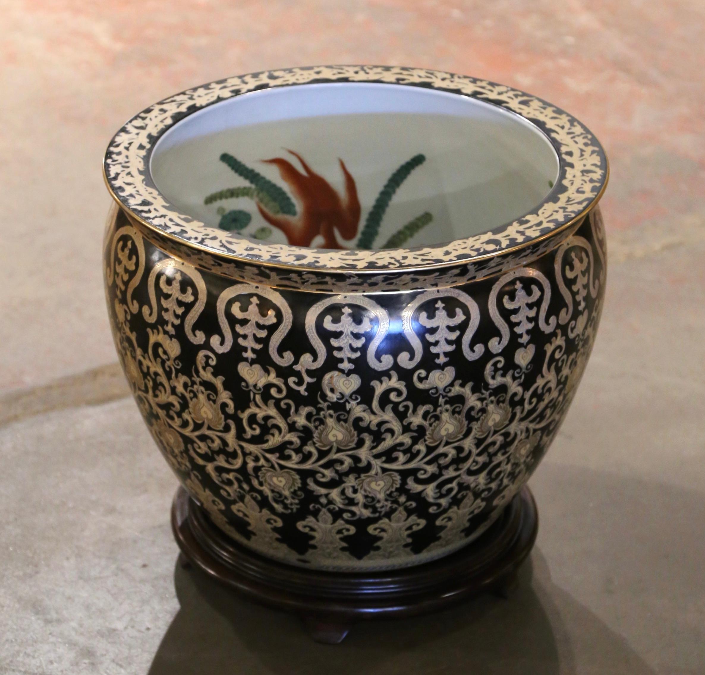 This vintage fishbowl was created in China, circa 1980. Round in shape and standing on a carved fruitwood base, this elegant porcelain planter features hand painted floral and leaf motifs throughout. The ceramic vase is painted on the inside as well