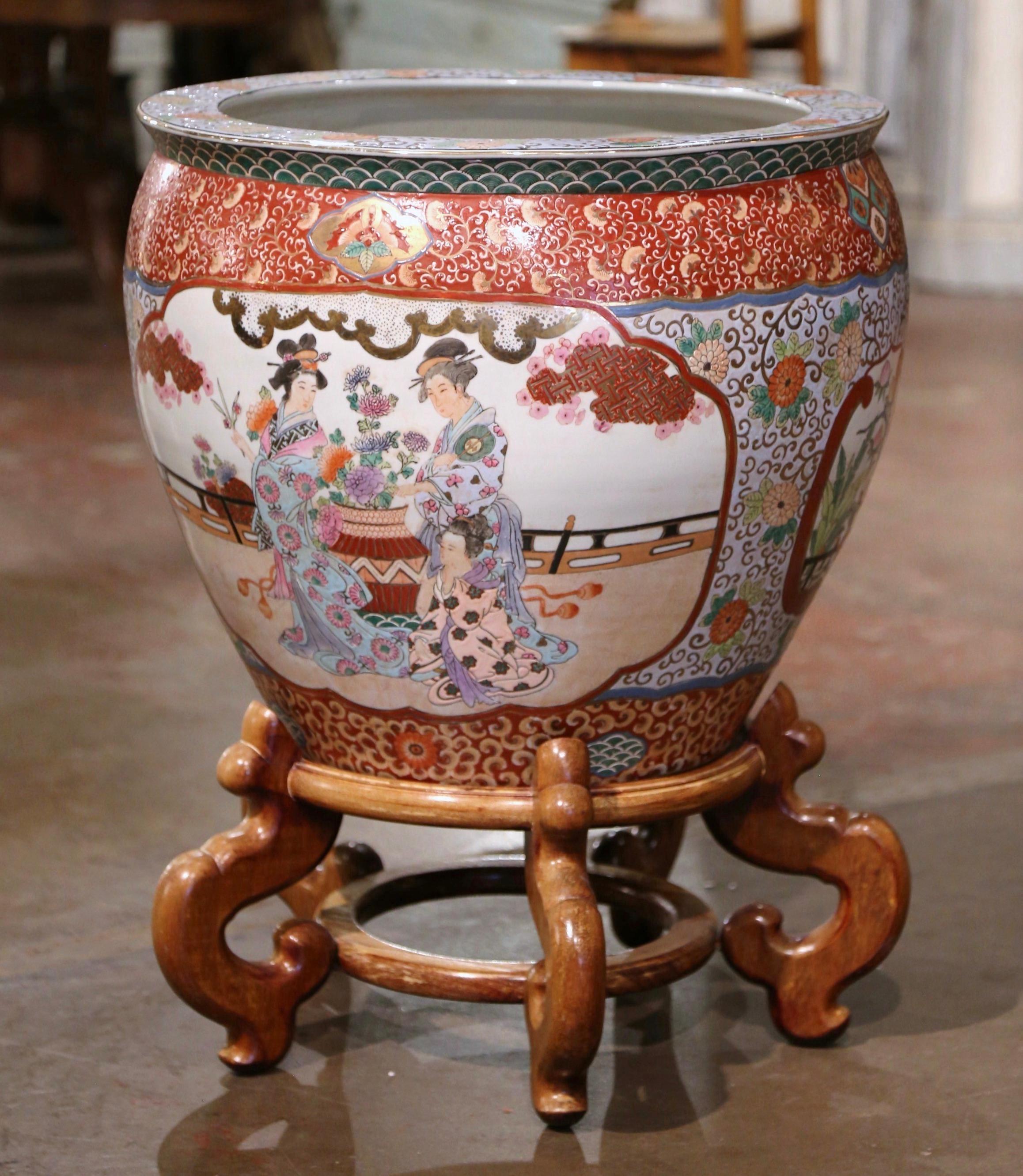 This massive and colorful vintage fishbowl was created in China, circa 1970. Round in shape and standing on a carved fruitwood base, this elegant exotic porcelain planter features two large hand painted medallions with Chinese figural motifs and