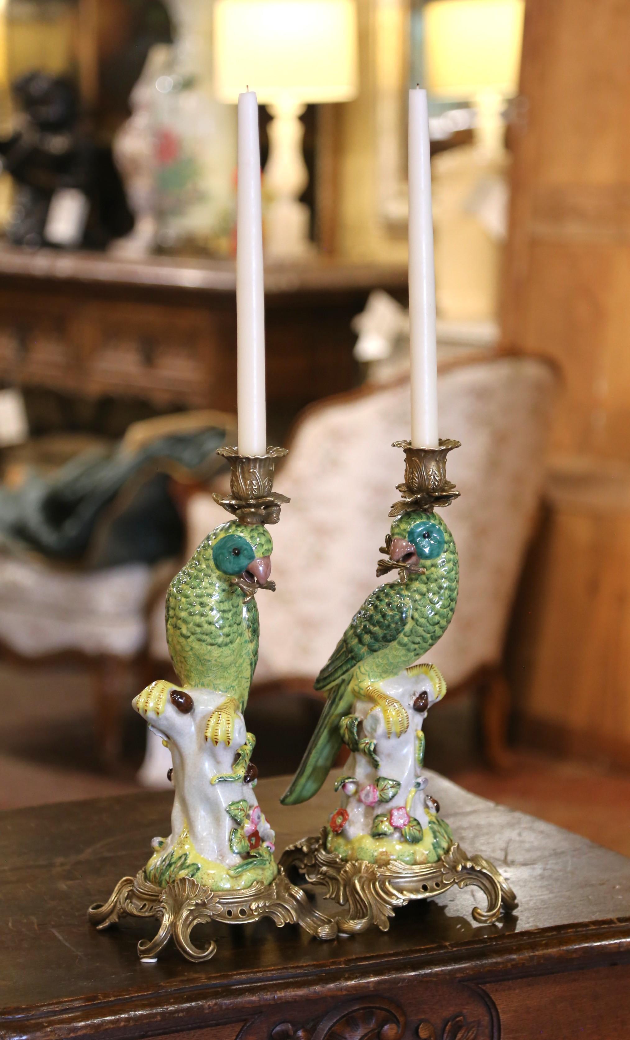 This whimsical pair of mid-century candlesticks was crafted circa 1950, likely for the Chinese export market, and features vividly painted porcelain parrots perched atop floral-covered tree stumps. Richly glazed in tones of emerald green, turquoise,