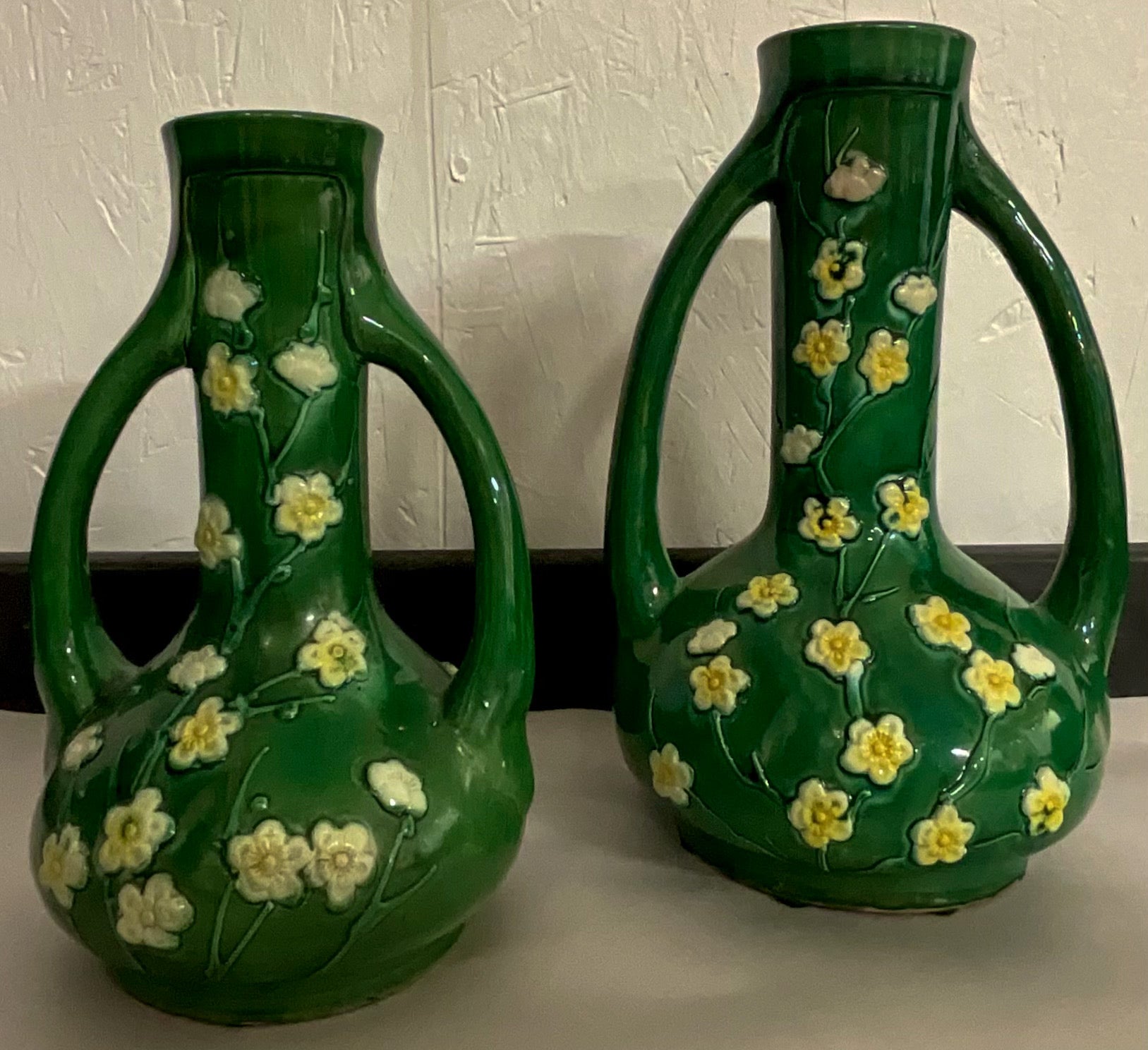 These is set of two Chinese Export style vases or ewers. They are a vivid green majolica glaze with a spraying of white blossoms. Measures: Small ; 5.25”H x 8.5”H.