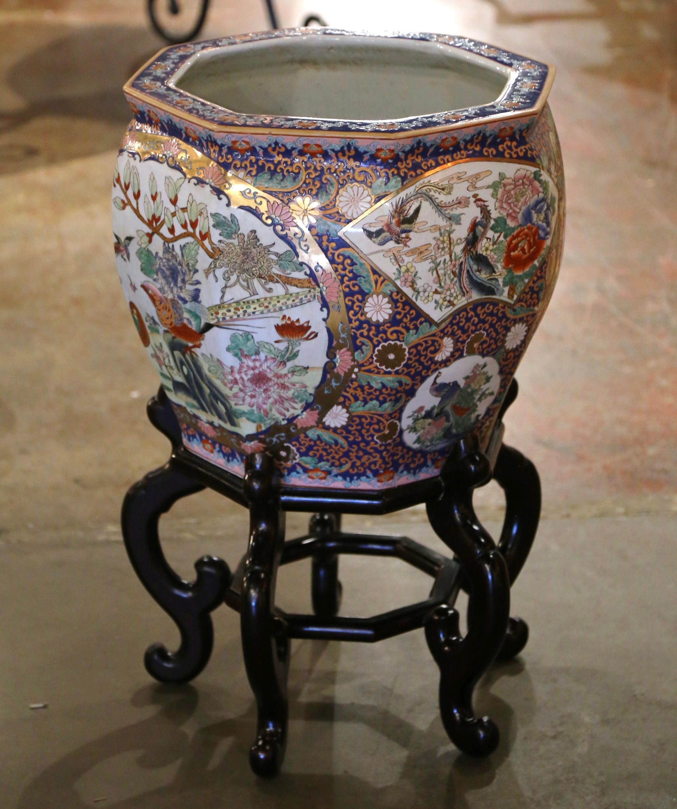 Questa grande e vivace boccia per pesci d'epoca, realizzata in Cina intorno al 1970, è un esempio lampante della tradizionale arte della porcellana cinese. Di forma ottagonale e graziosamente appollaiata su una base in legno di frutta intagliato,