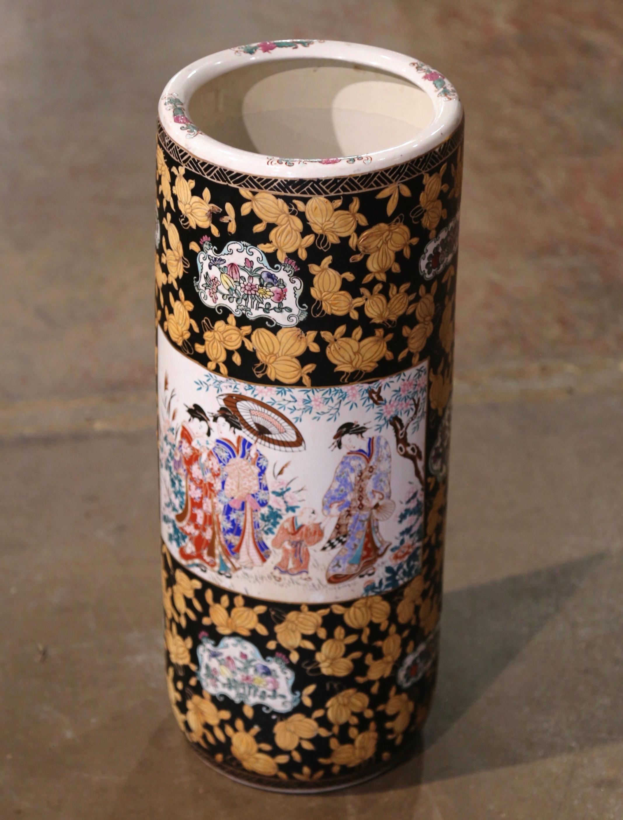 Created in China circa 1950, this large colorful Famille Rose umbrella stand is round in shape and features hand painted medallions with Chinese people in traditional clothing; it is further embellished with floral and foliate motifs on a black