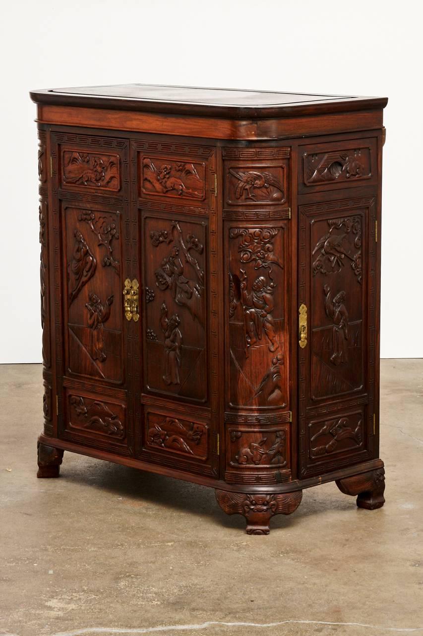 Fantastic midcentury Chinese carved rosewood dry bar liquor cabinet. Features a large flip top panel that opens to reveal two handles that lift out the bottle caddy. There are bottle racks, corner drawers, corner doors, and small hidden drawers. All