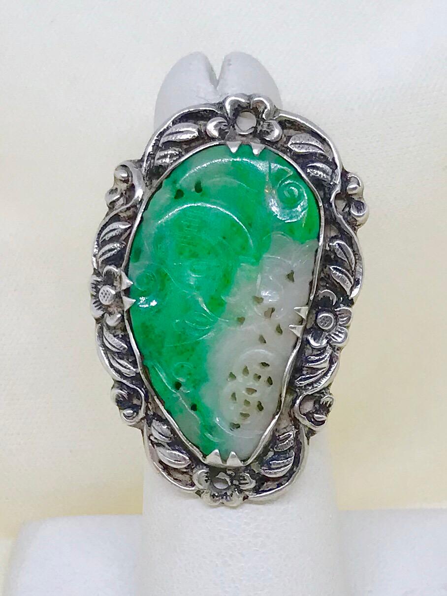 Circa 1940s Chinese sterling silver ring set with green variegated jade.  The Sterling setting is in an ornate floral and leaf design bezel set with hand-carved green and white jade.  The top of the ring measures 1.5