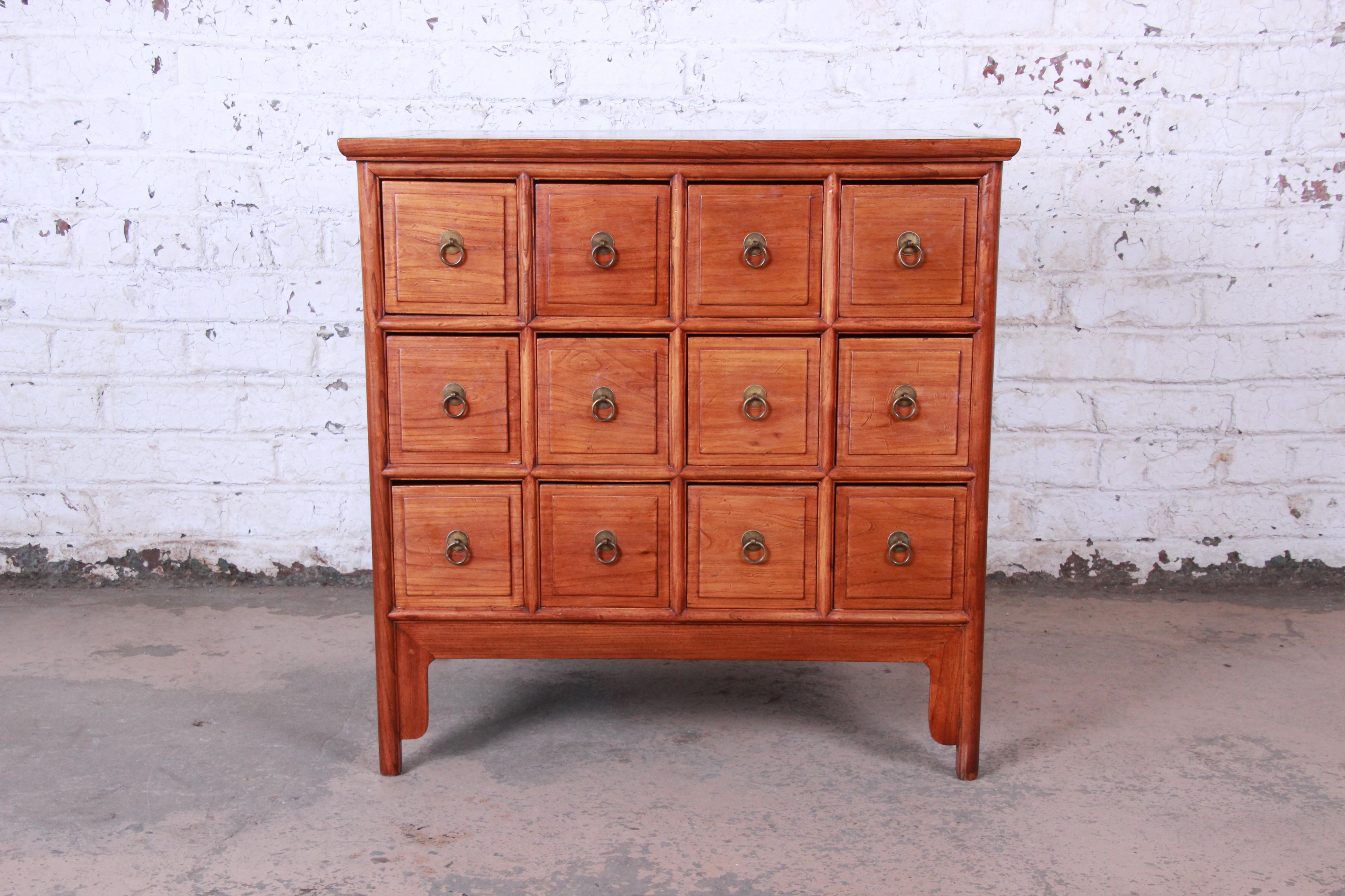 A stunning midcentury Chinese twelve-drawer apothecary cabinet. The chest features gorgeous elm wood grain and a nice subtle Asian design. A unique herbal pharmacy chest with a tapered form that is supported by square legs with shaped aprons. It