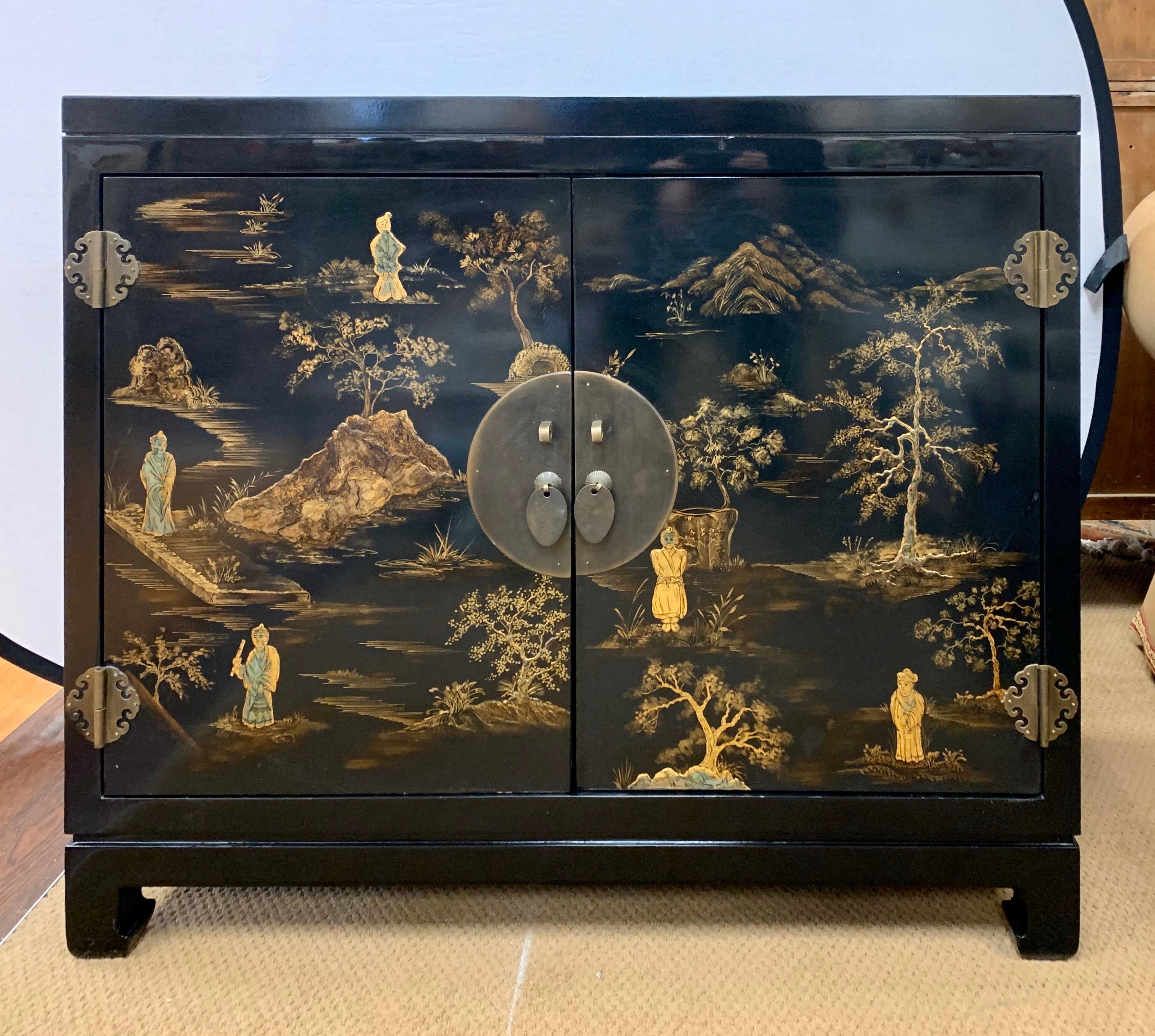 A stunning Mid-Century Modern black lacquer cabinet with raised chinoiserie gilt landscape scenes and brass handles on the double doors that open to multiple shelves and drawers inside. This is a substantial, heavy cabinet, with exceptional