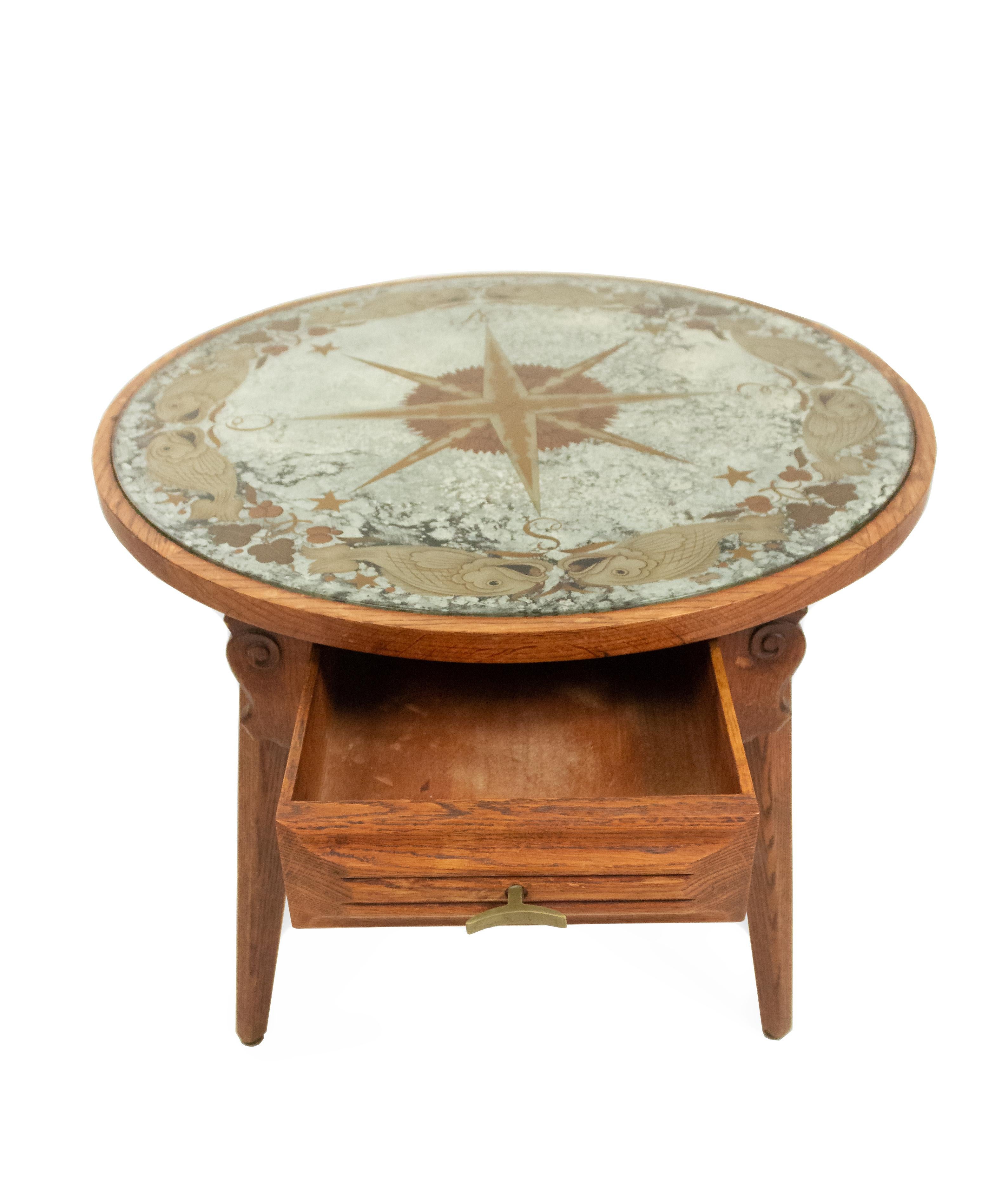 French midcentury coffee table with a carved ash wood base on 4 splayed feet with a drawer having a brass pull supporting a round églomisé inset mirrored top decorated with a center compass.