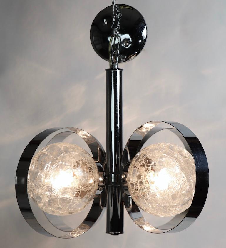 Stylish and chic hanging fixture having exaggerated circular chrome bands which surround clear crackle glass ball globes. The chandelier has 4 globes, it is in clean, original and working condition, showing only light cosmetic wear, normal and