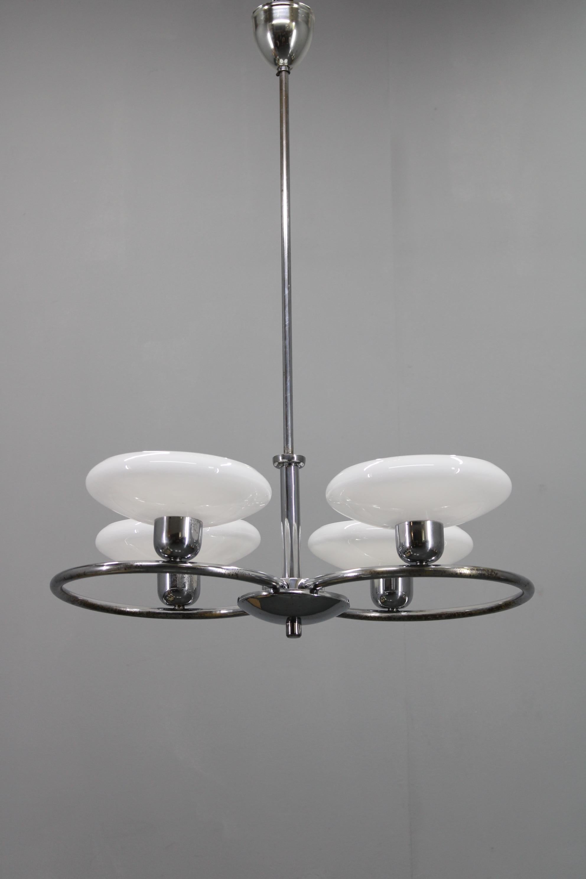 Elegant Mid-Century chrome chandelier produced in 1950s Czechoslovakia, distinguished by its four large milk-glass disc shades arranged on a circular chrome structure. The refined balance of reflective metal and soft opaline glass captures the