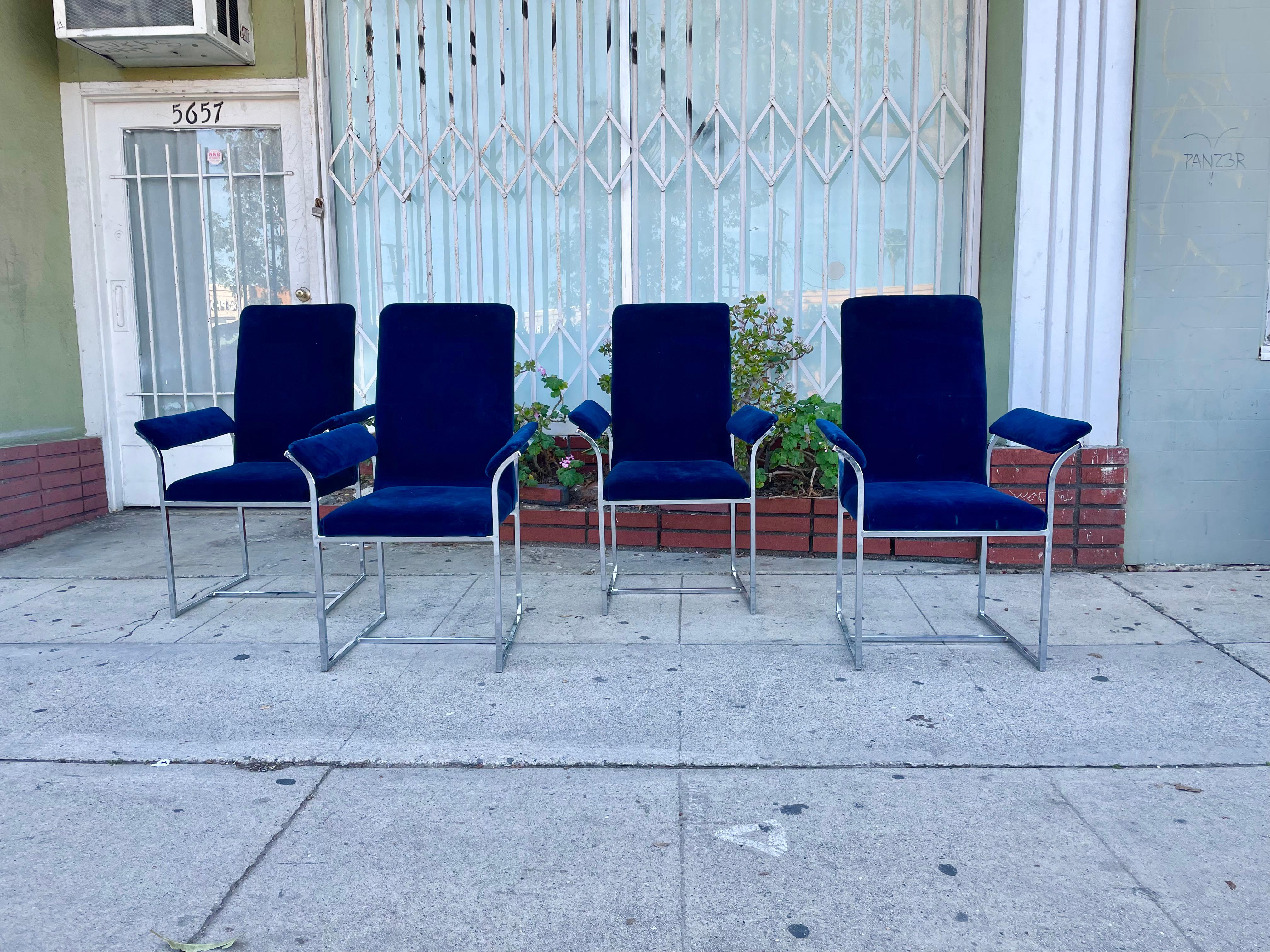 Vier verchromte Esszimmerstühle im Stil von Milo Baughman. Jeder Stuhl hat ein verchromtes Gestell mit einer einzigartigen skulpturalen Armlehne und ist mit blauem Samt gepolstert, was ihn zu einem Unikat macht.