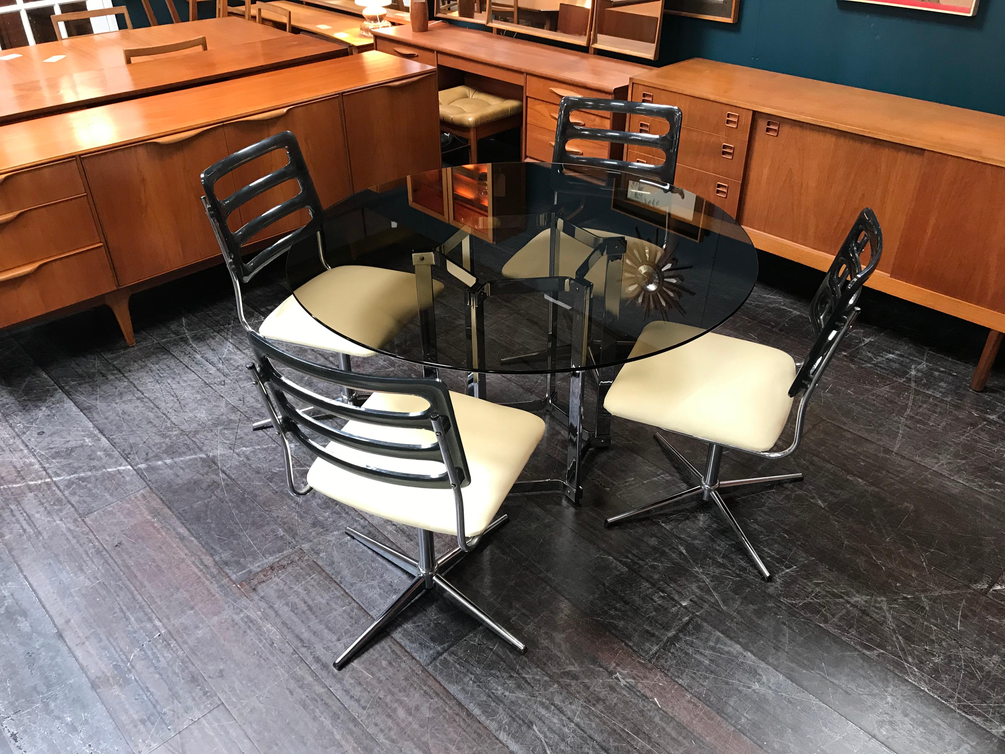 This Merrow Associates circular glass table with chrome base comes with 4 chairs with star bases and vinyl seat pads. The table was designed for Merrow, circa 1971, by Merrow’s founder, Richard Young. A former Royal College of Art student, he later