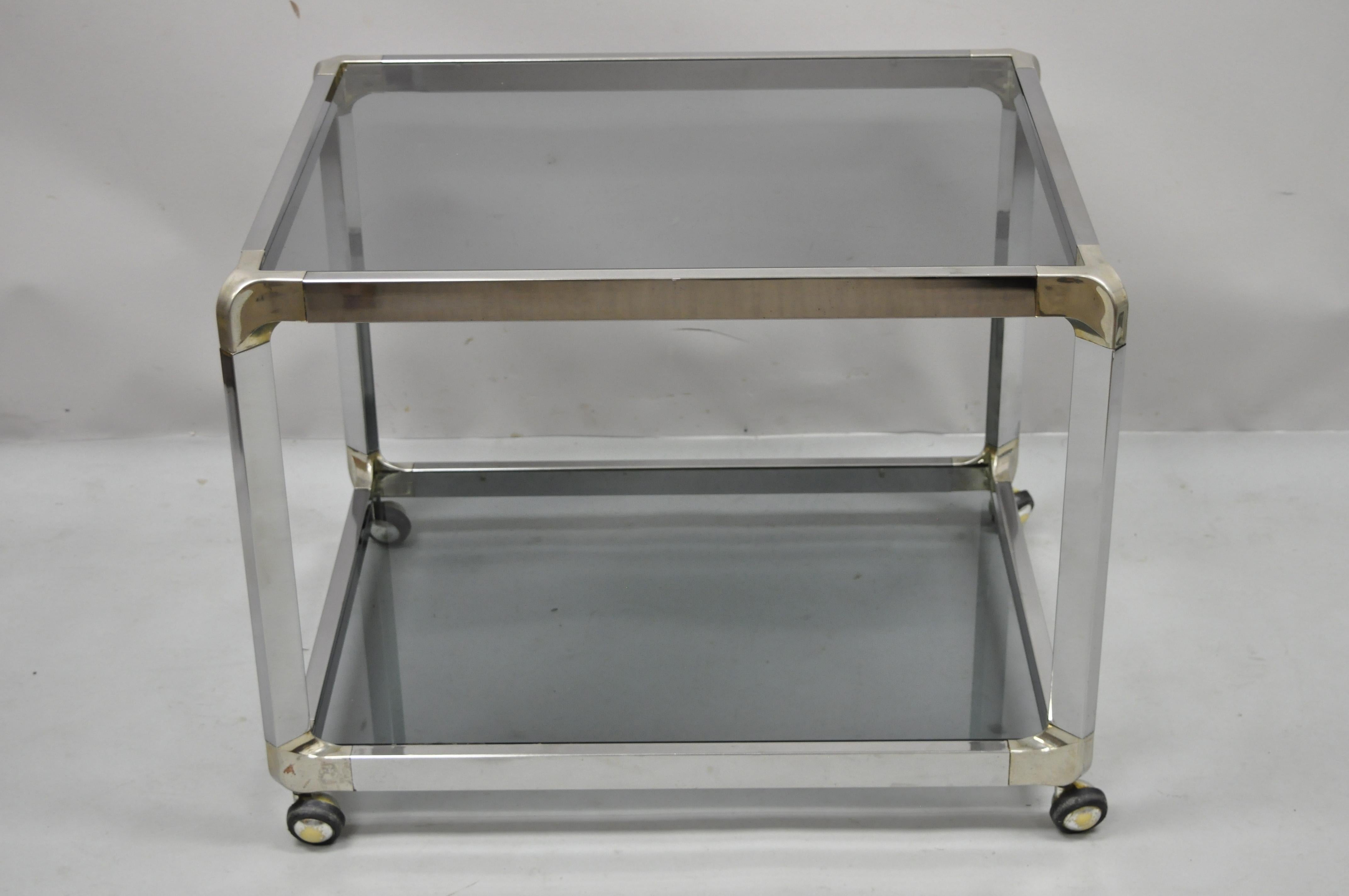 Mid-Century Modern chrome smoked glass rolling bar cart occasional side table on wheels.Item features rolling casters, 2 tiers of smoked glass, brass tone accents, clean modernist lines, great style and form. Circa 1970s. Measurements: 22
