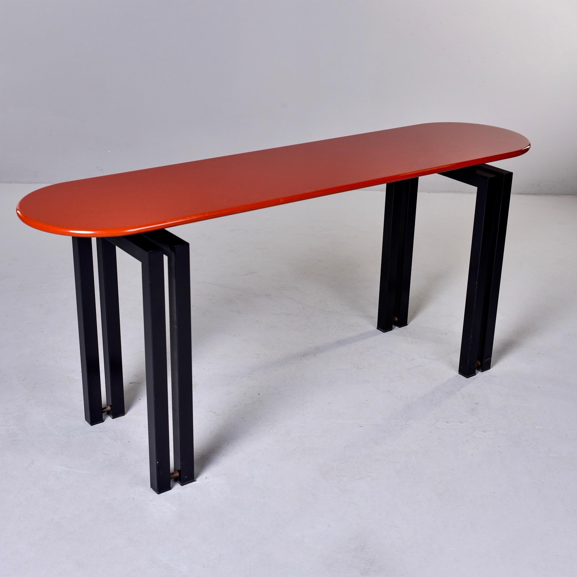 Circa 1980s console by Cidue of Italy features an oval table top with a cinnabar color lacquered top and contrasting black metal base / legs. Marked with maker’s tag on underside of top.