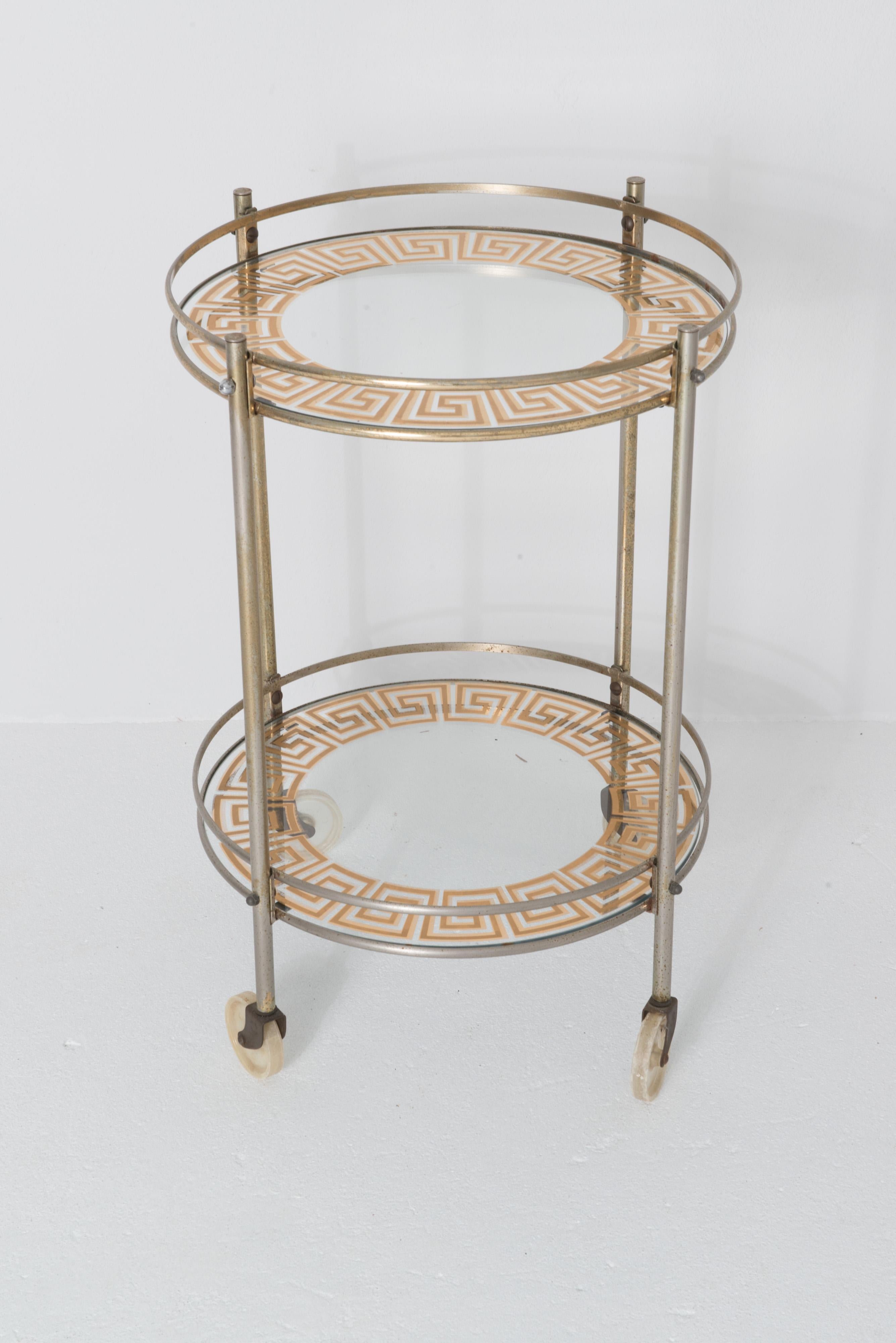 Mid century modern circular Greek Key glass and brass bar cart with clear plastic caster wheels.