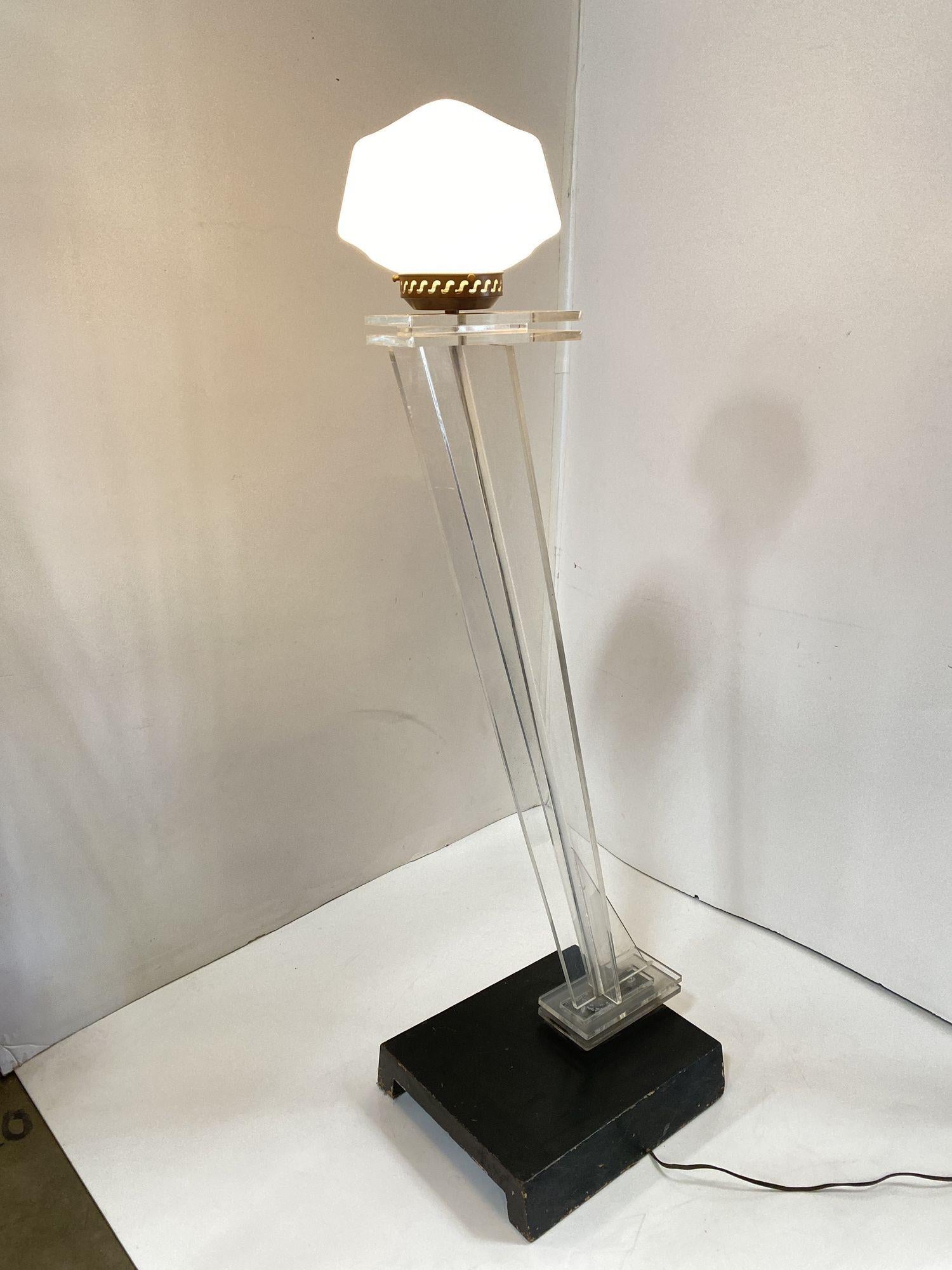 Hand-made abstract Mid-century floor lamp featuring a slanted clear Lucite sculptural fixed to a black lacquered wood base with a white schoolhouse glass lamp shade.
 
Circa 1950.