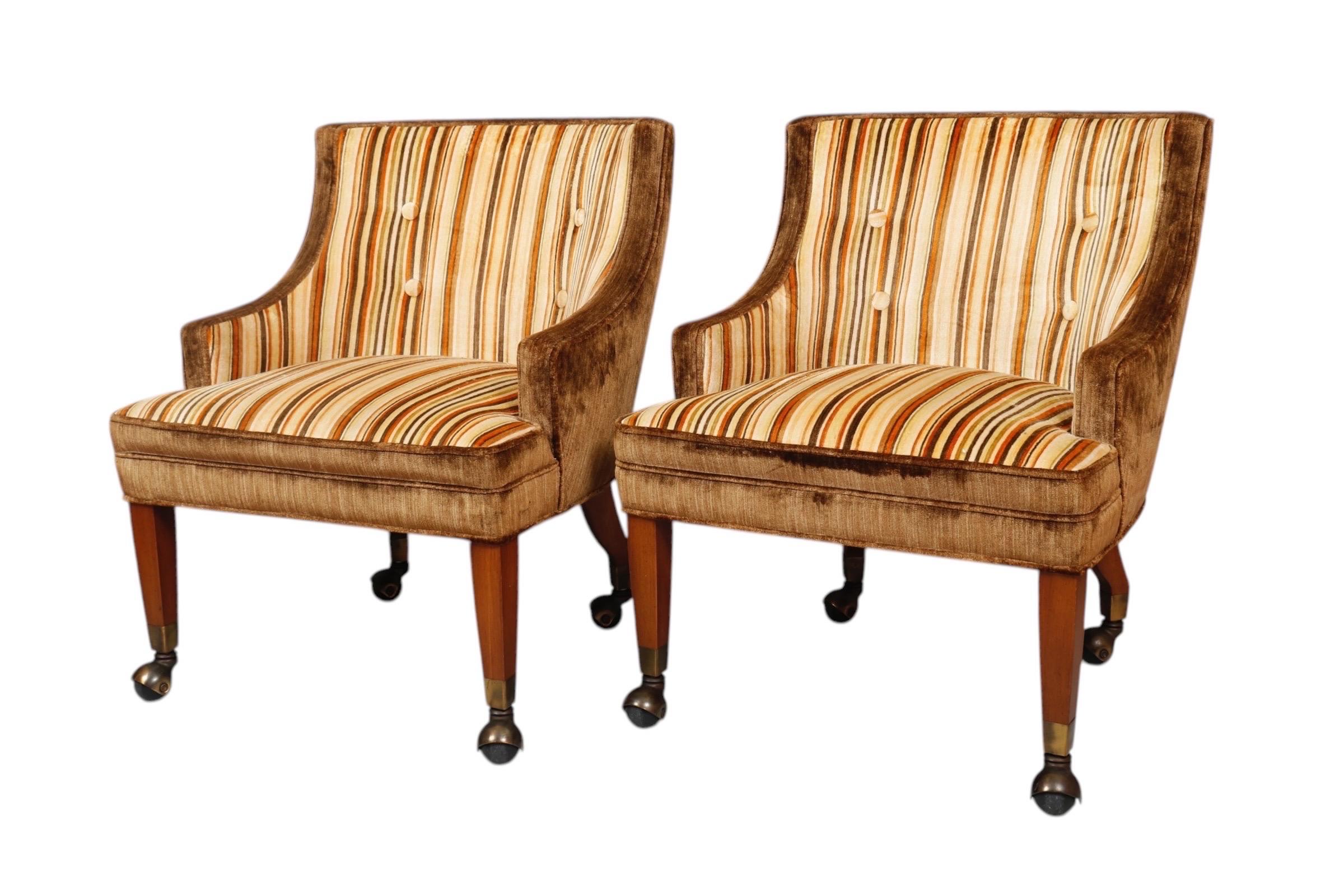 A pair of mid century modern club chairs, circa 1960. Curved low backs and short arms frame horseshoe shaped seats. The seat in front is upholstered in a midcentury striped velvet in cream, brown, orange, and chartreuse. The outside back is