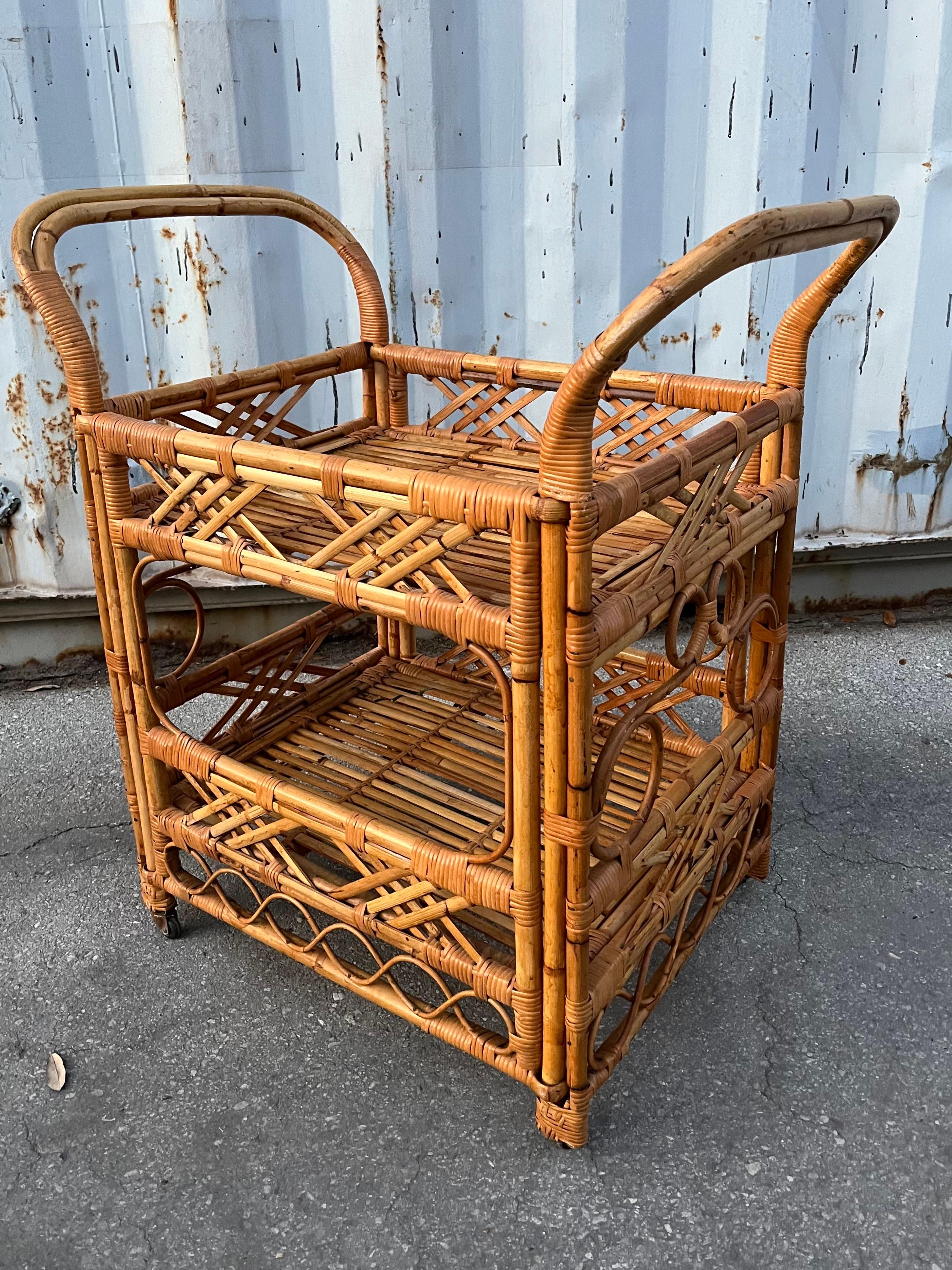Vintage Mid Century Coastal Style Rattan Dry Bar/ Serving Cart in the Franco Albini's Manner.  Circa 1970s
Features a two-tiered frame with ornate accents and handles at both sides.
In excellent original condition with minor signs of wear and age.