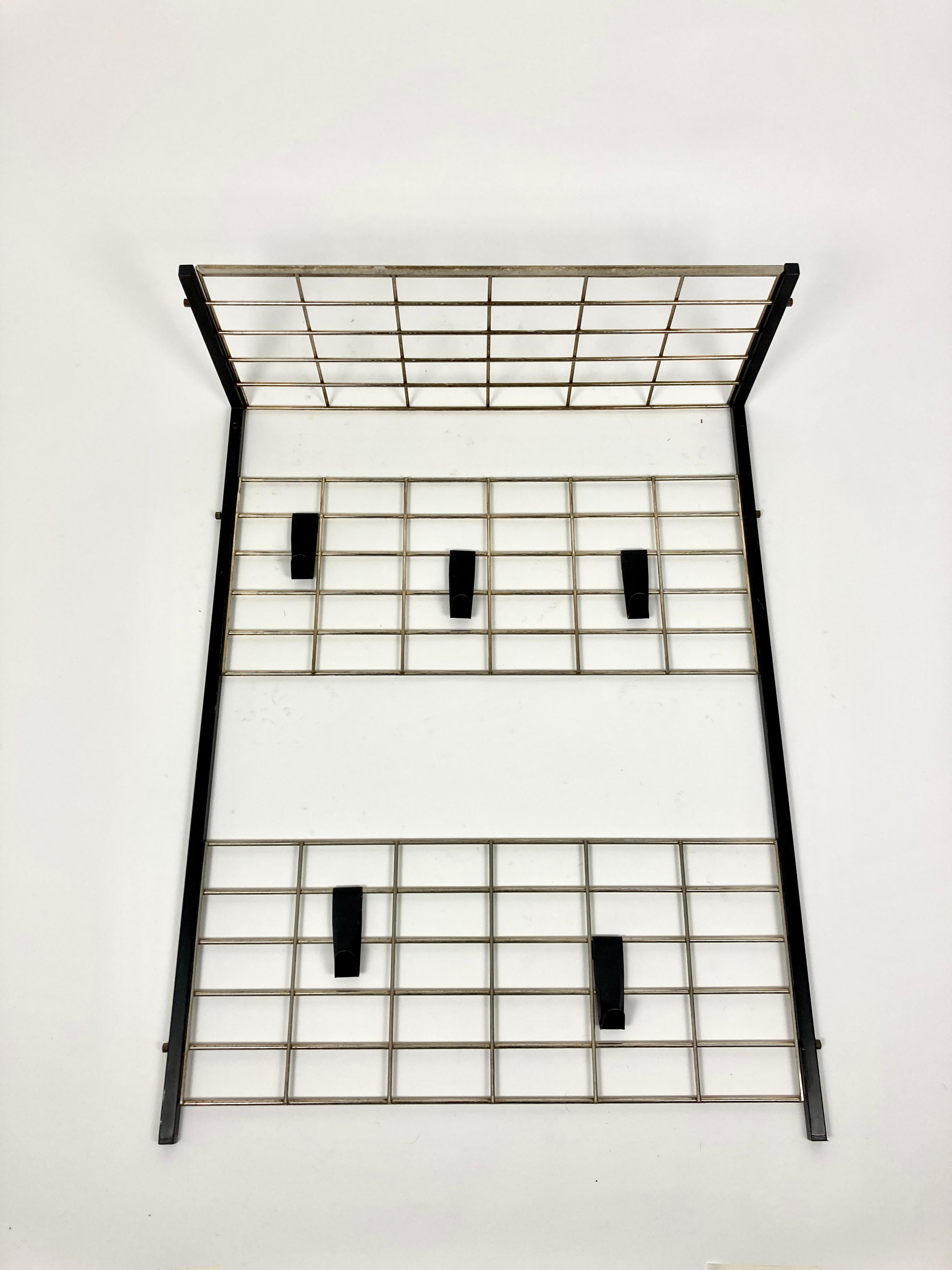Mid-century coat rack, Netherlands, circa 1950-60 in the manner of Coen de Vries for Pilastro.

Great modernist Dutch design piece. Minimalist yet functional.

Black steel frame with brass grid sections and hat shelf. 5 black hooks which can be