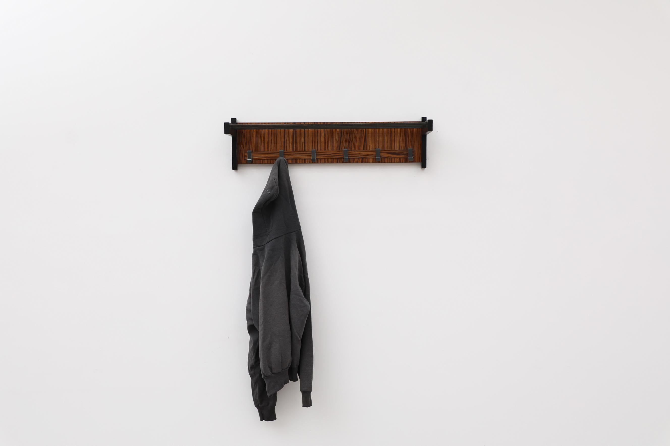 This wall mounted coat rack features 6 hooks on an cocobolo back with a metal hat rack and frame. It's in original condition with wear that's consistent with its age and use. Other wall mounted coat racks are available and listed separately.